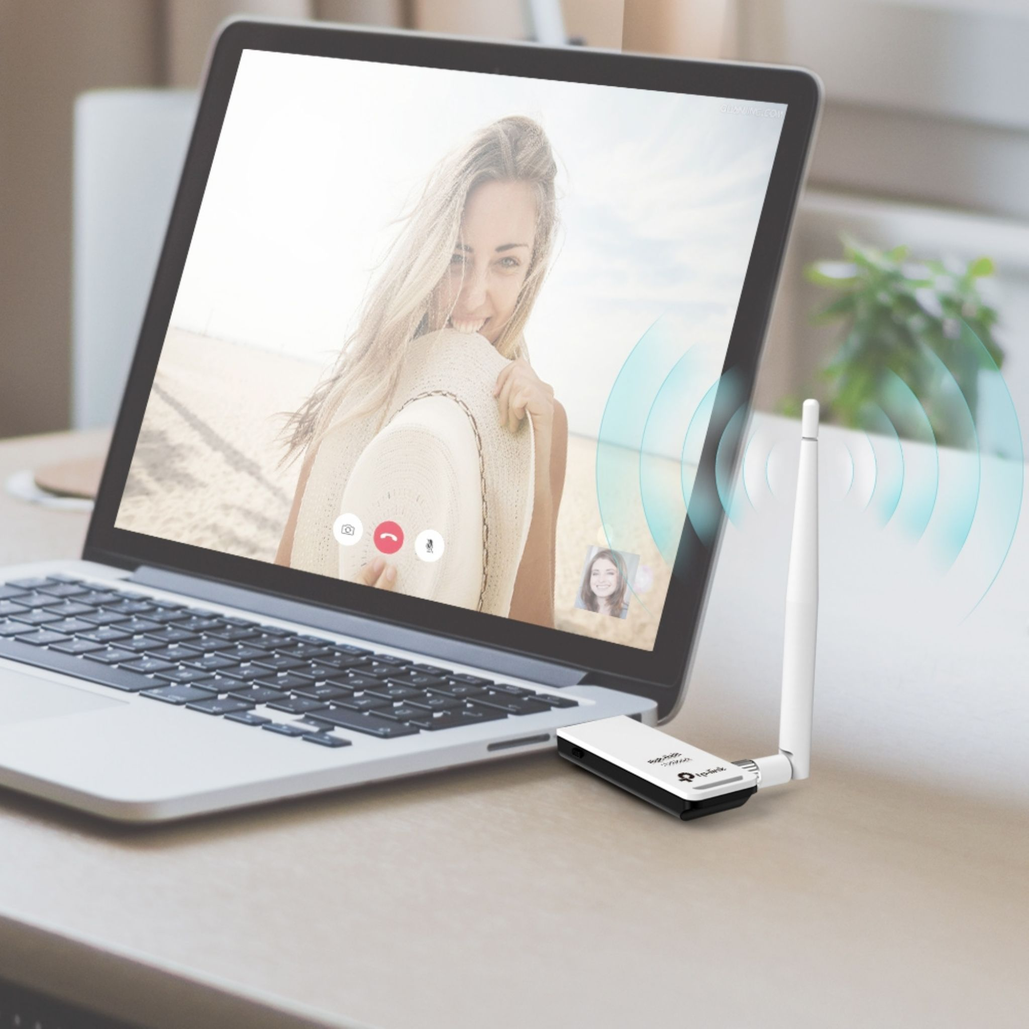 Ordinateur portable ouvert avec un appel vidéo à l'écran. Un adaptateur wifi est sur la table. Fond blanc.