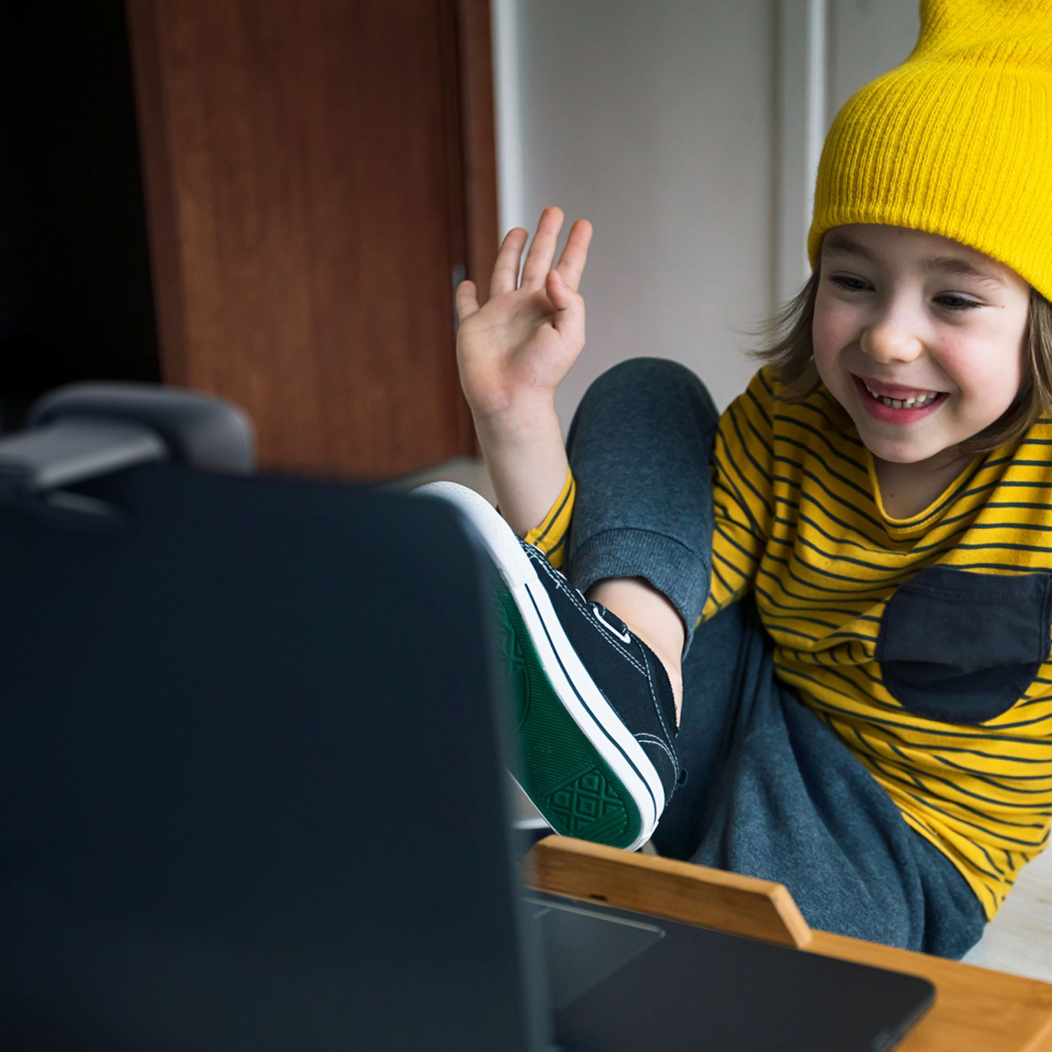 Mały chłopiec w żółtej czapce macha do laptopa. Tłem jest pokój.
