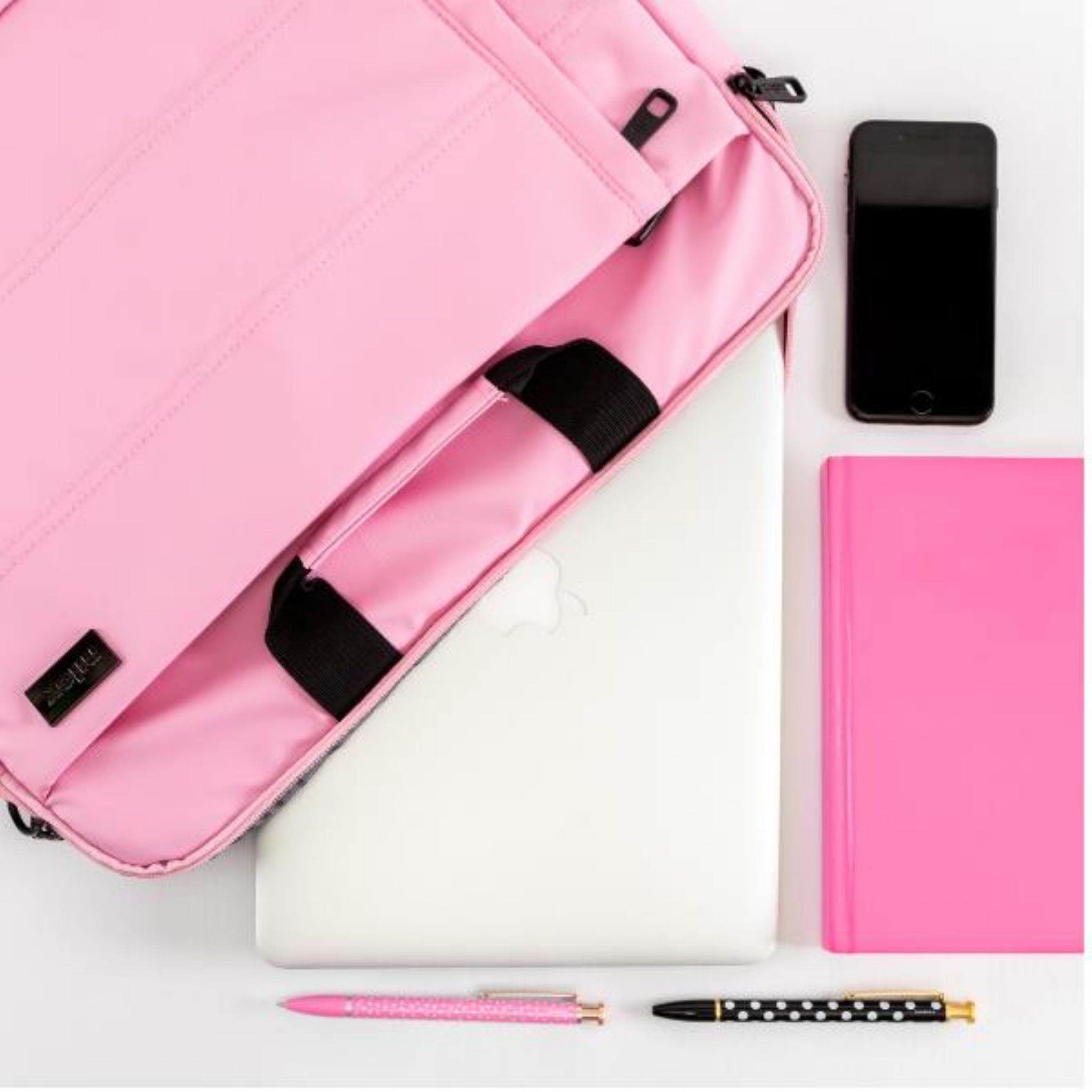 Una bolsa rosa para portátil abierta, con portátil, bolígrafo, teléfono, cuaderno y calcetín.