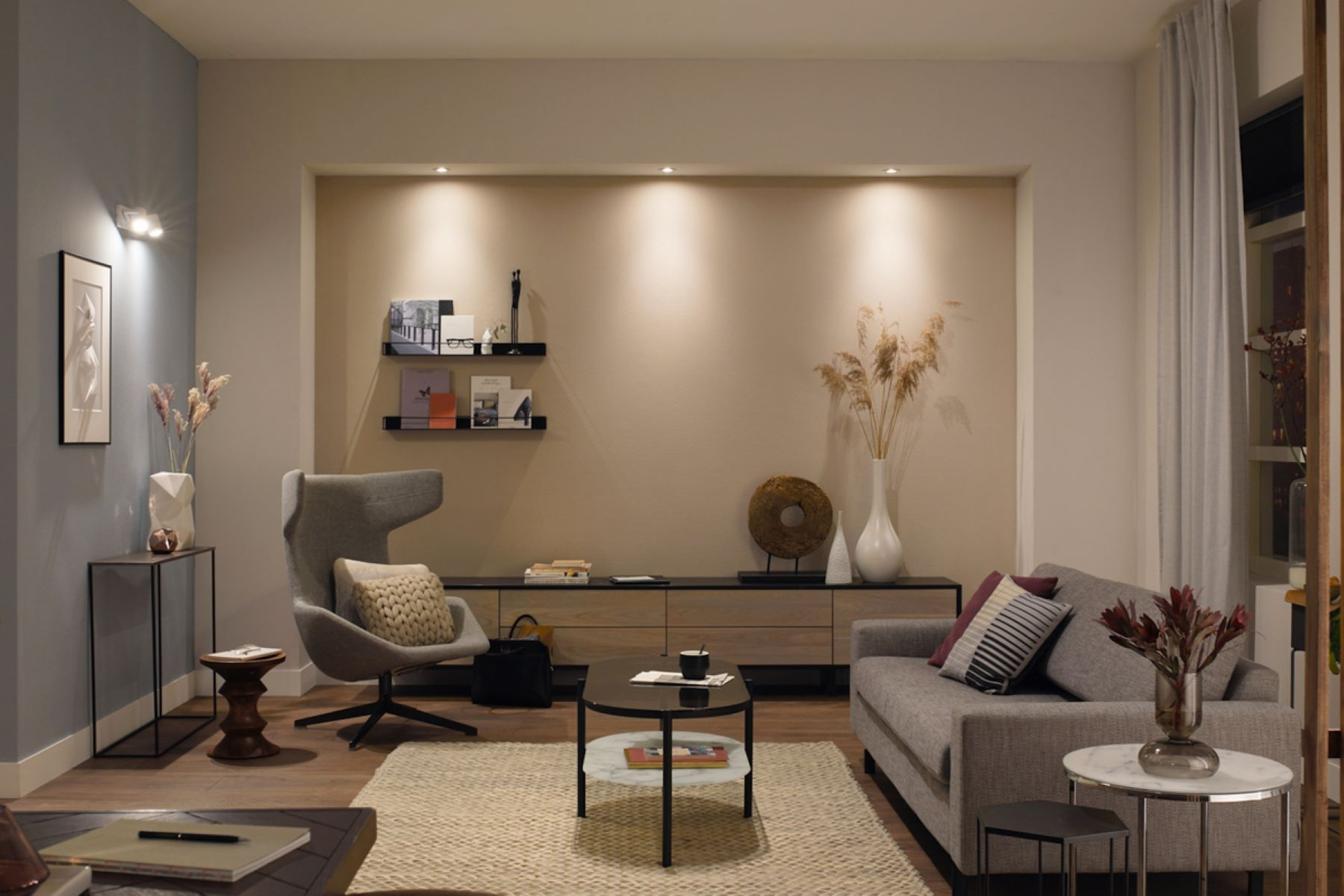 Salón con esquema de color neutral. Sofá gris, sillón, mesa de centro. Iluminación y elementos decorativos.