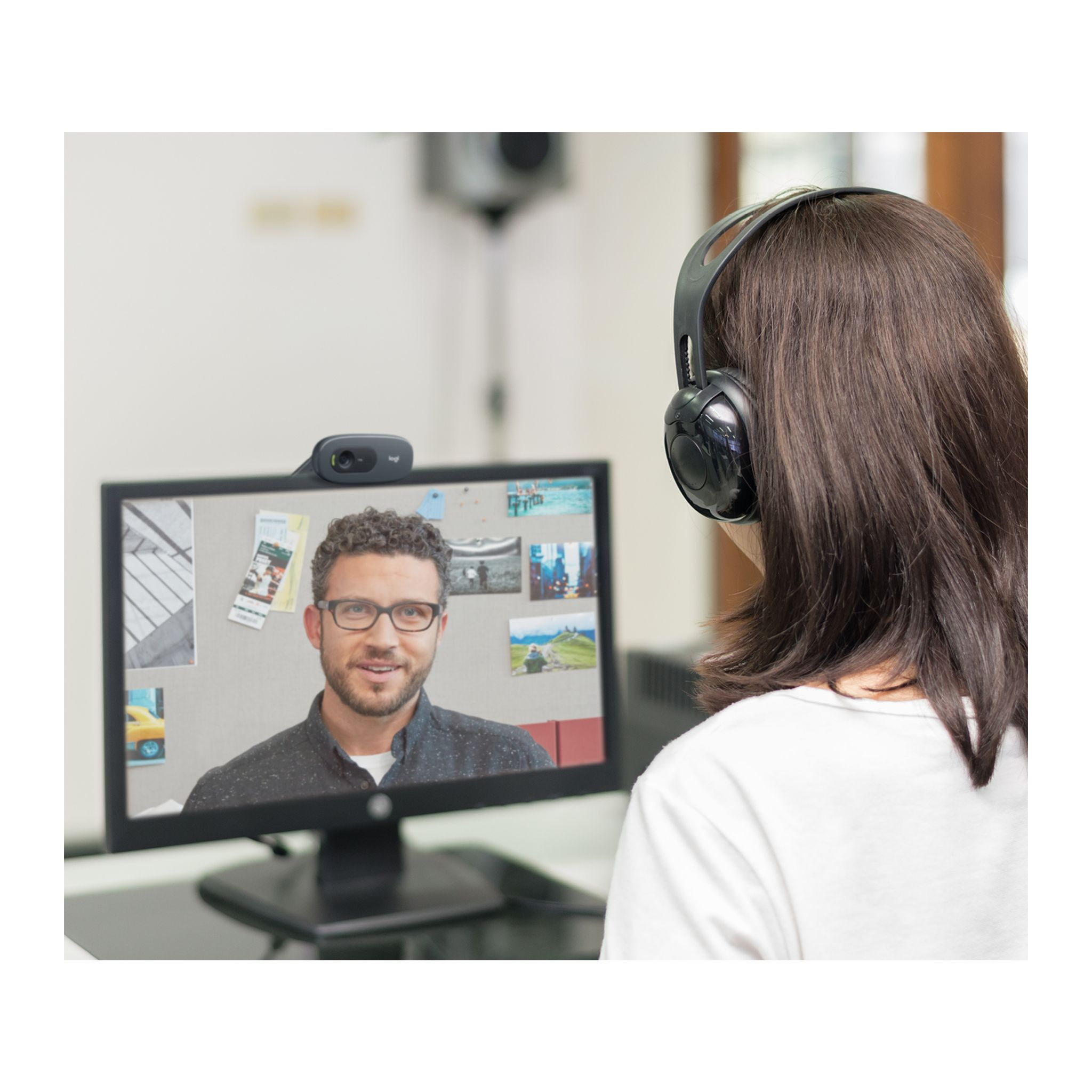 Kobieta ze słuchawkami podczas rozmowy wideo. Mężczyzna na monitorze. Białe tło.