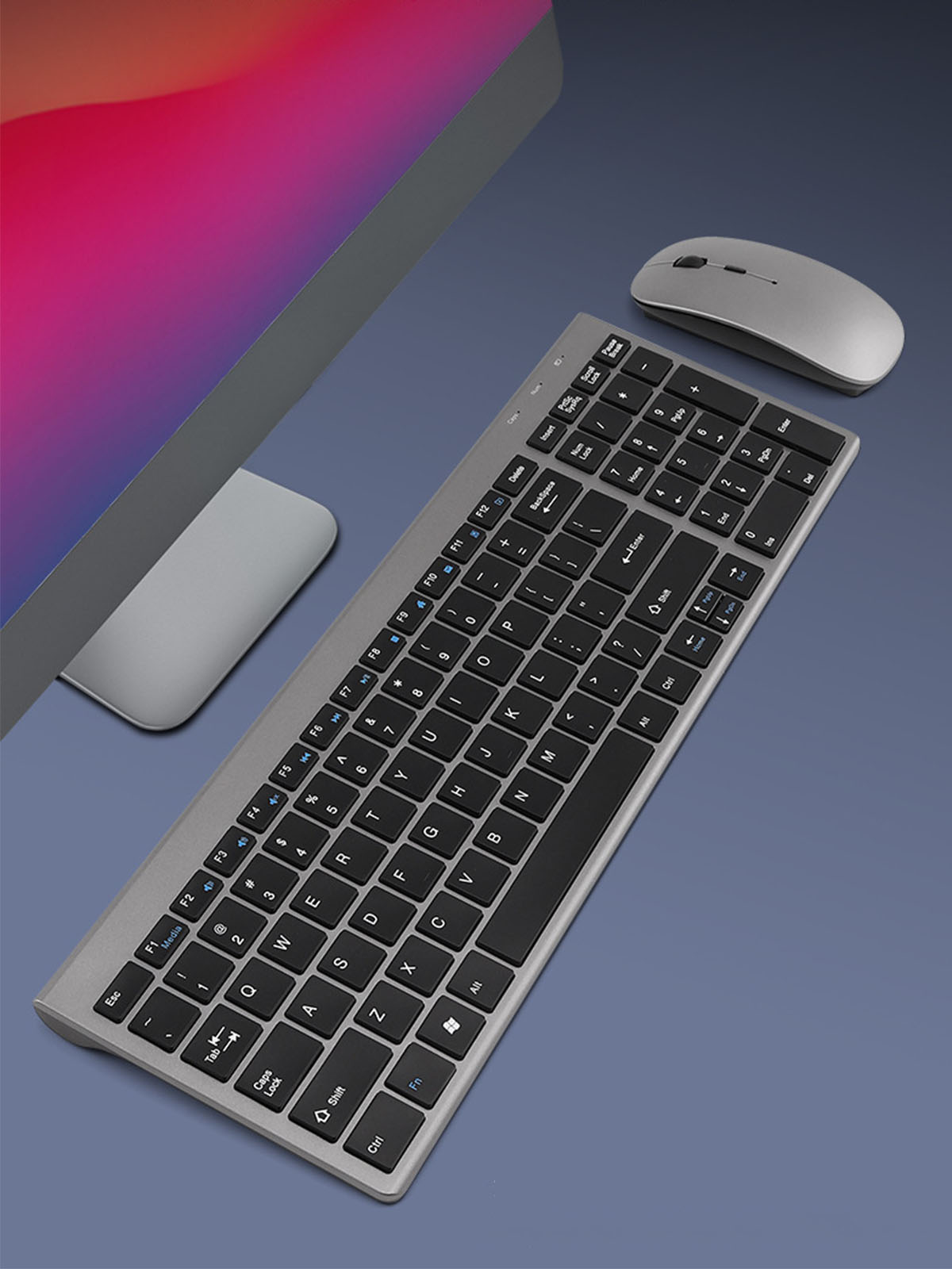 Silberne Tastatur und Maus auf blauer Oberfläche. Monitor im Hintergrund.