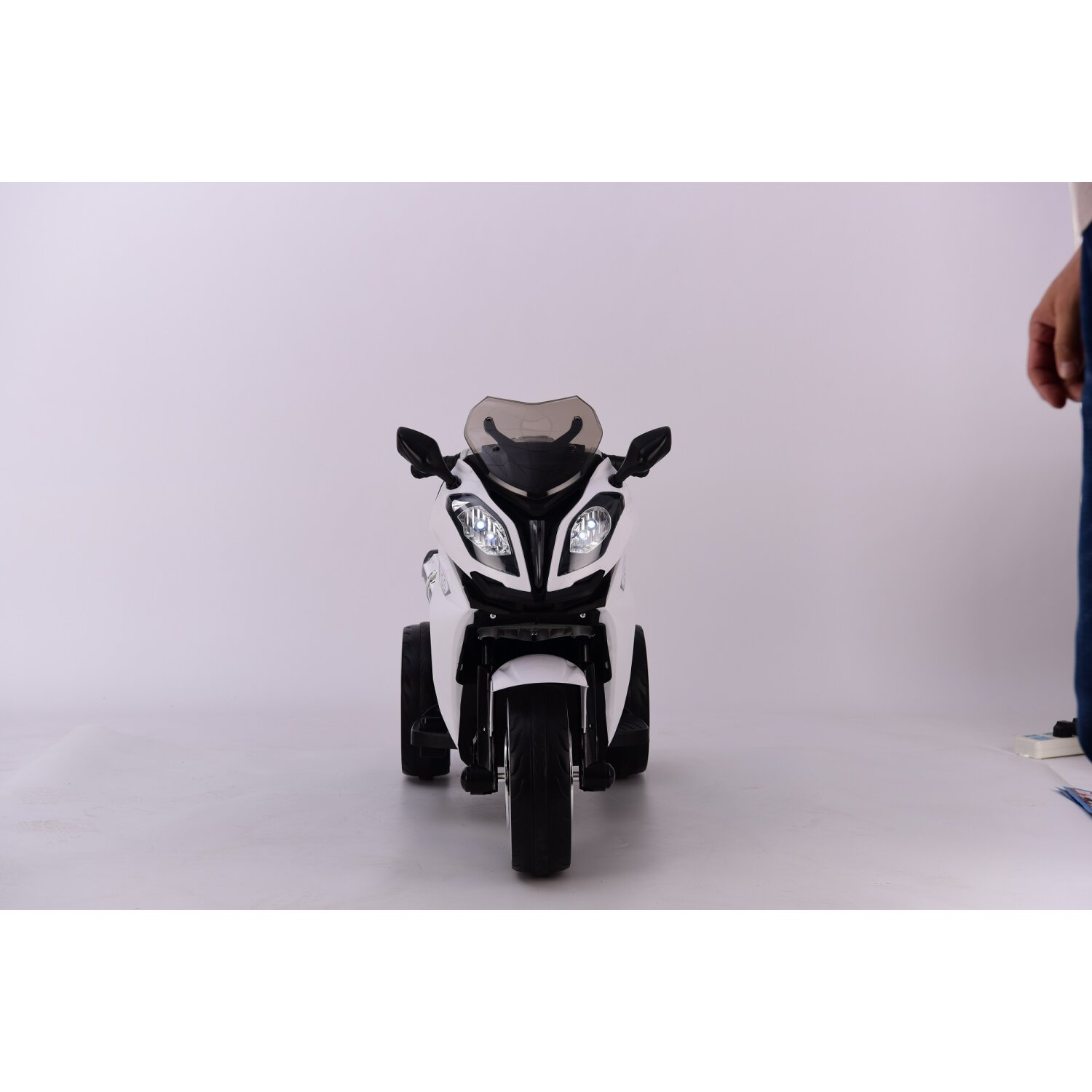Ein weißes Spielzeugmotorrad mit einer Person im Hintergrund.
