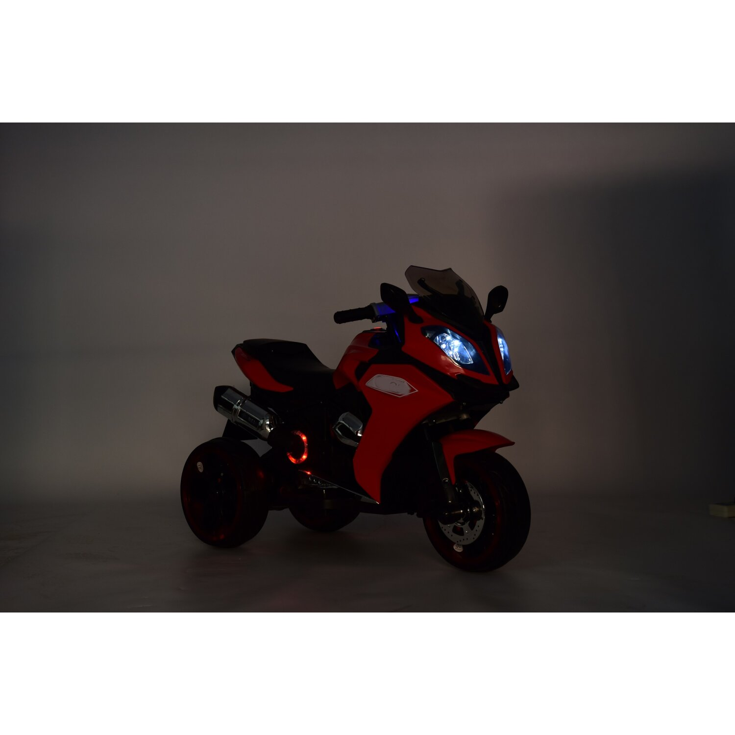 Ein rotes und schwarzes Spielzeugmotorrad mit Lichtern. Das Motorrad hat drei Räder und vor grauem Hintergrund.