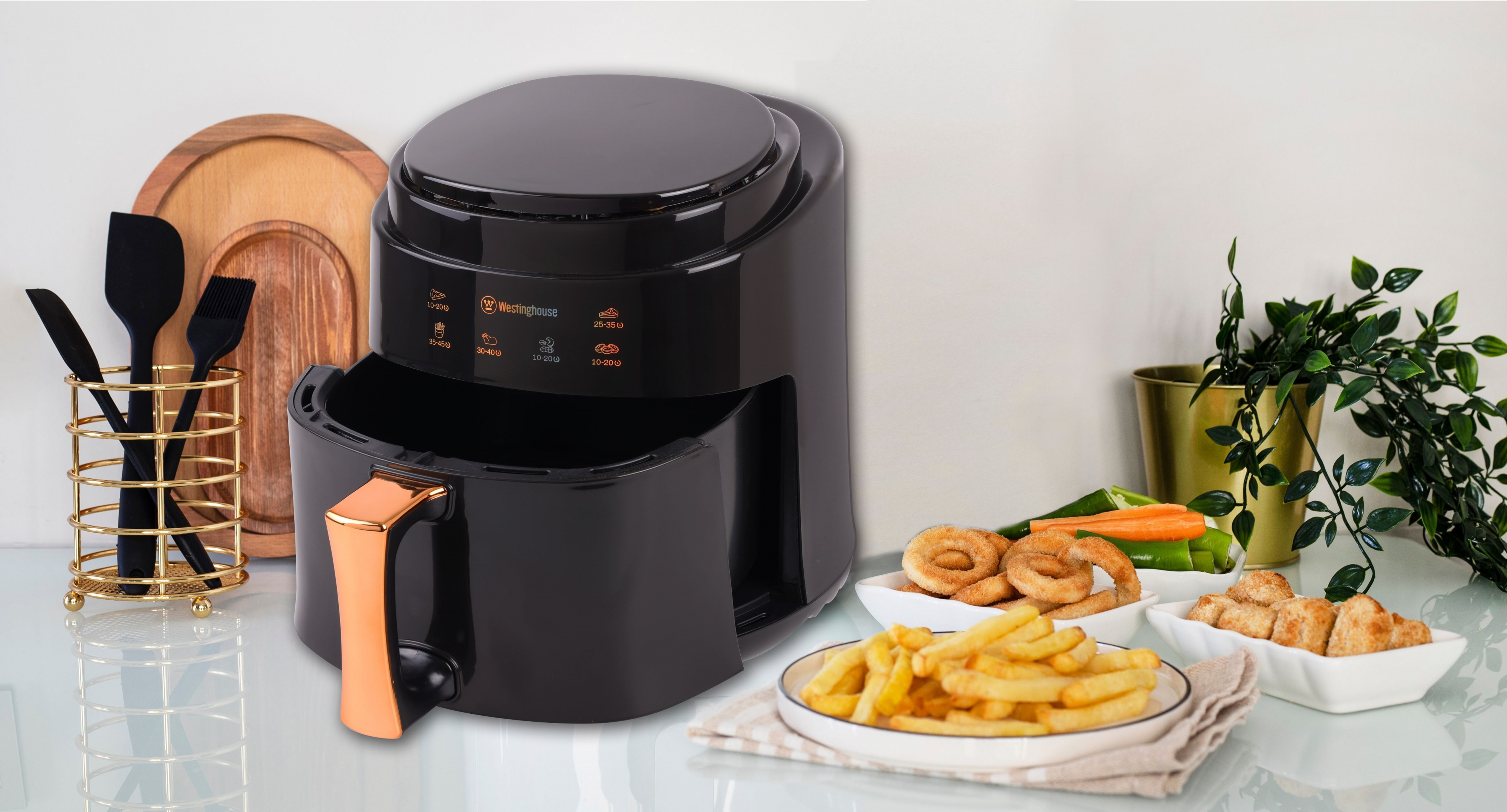 Schwarze Heißluftfritteuse mit Essen. Pommes, Zwiebelringe und Hähnchen auf der Theke.