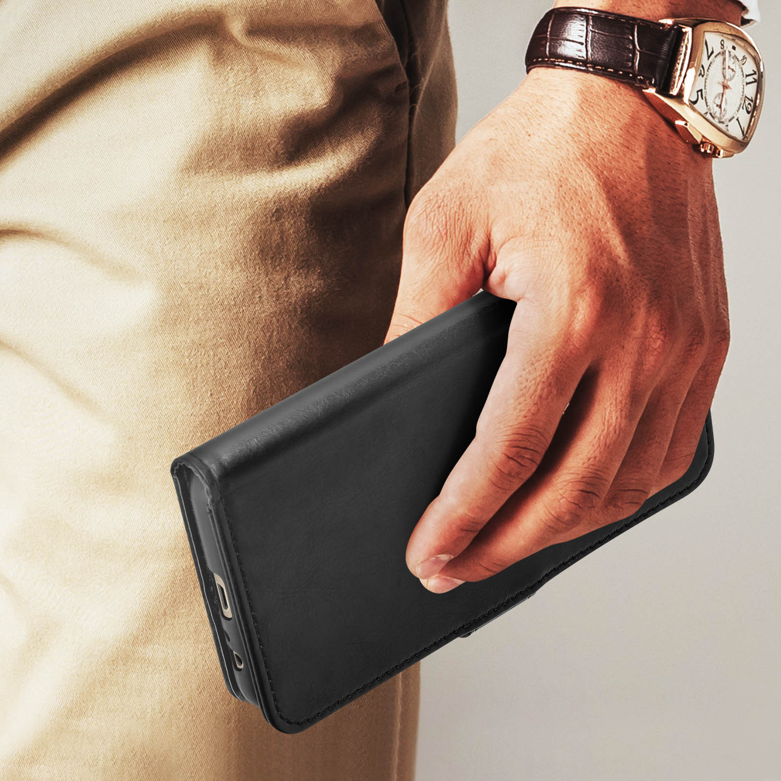 La mano di una persona che tiene una custodia nera per telefono, con un orologio al polso.