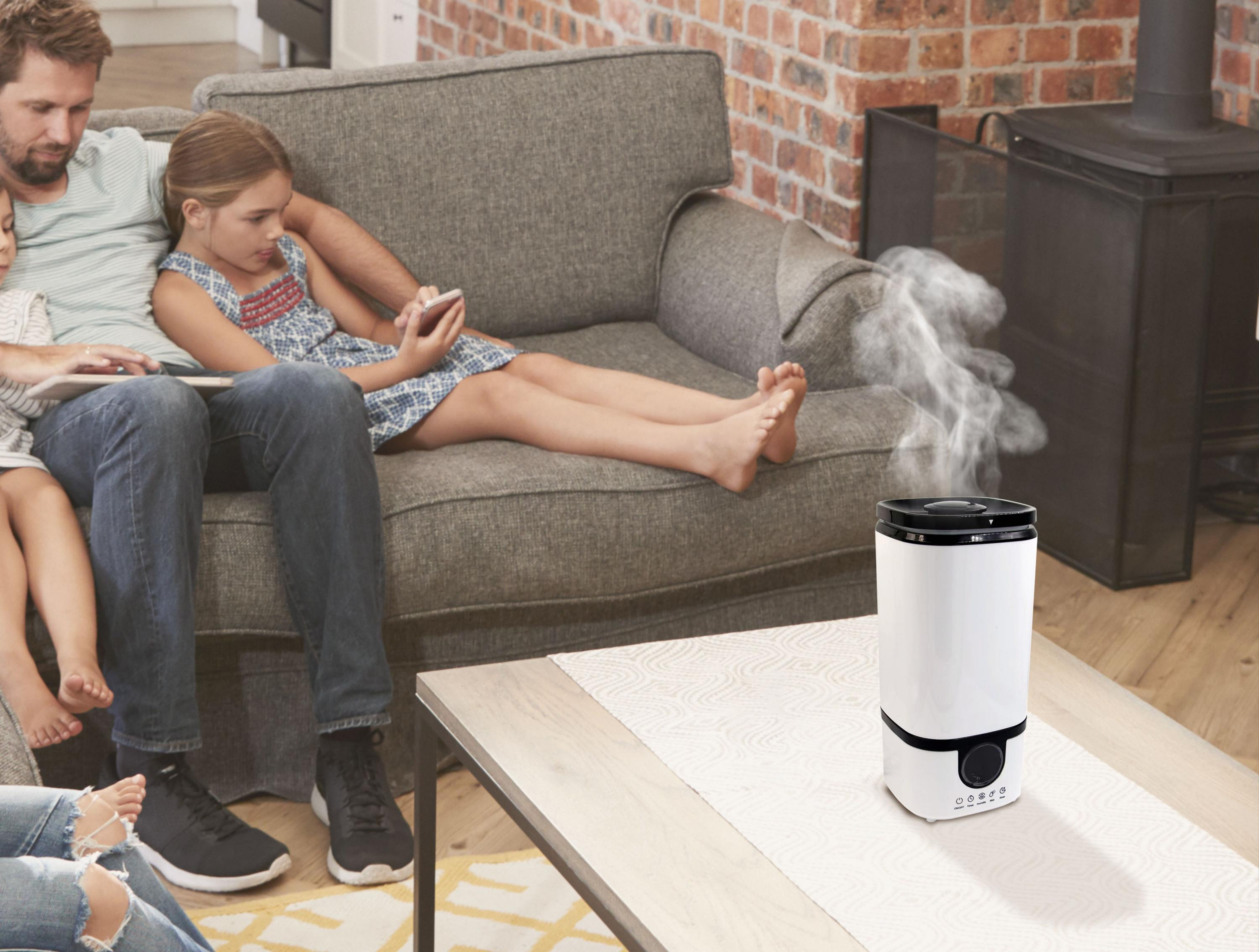 Personas en una sala de estar con un humidificador en una mesa, sale vapor.