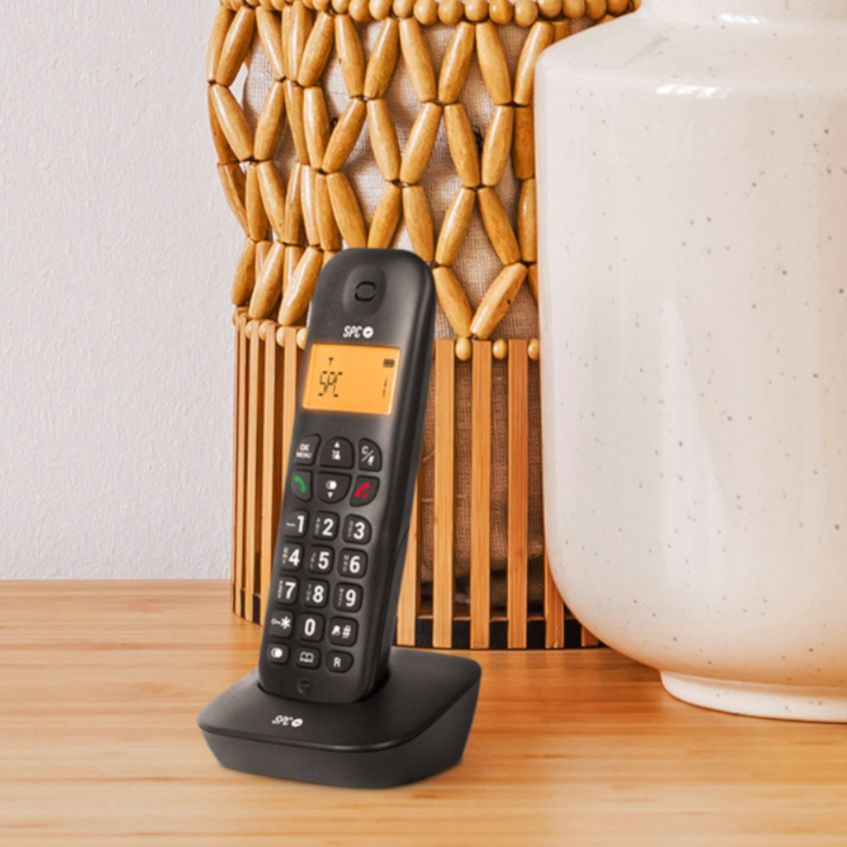Teléfono inalámbrico negro sobre base, mesa de madera y fondo de mimbre.