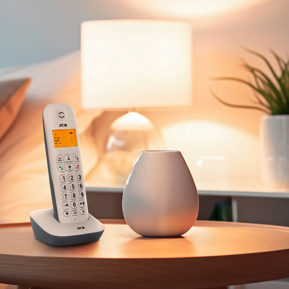 Un teléfono inalámbrico y un jarrón sobre una mesa de madera con una lámpara al fondo.