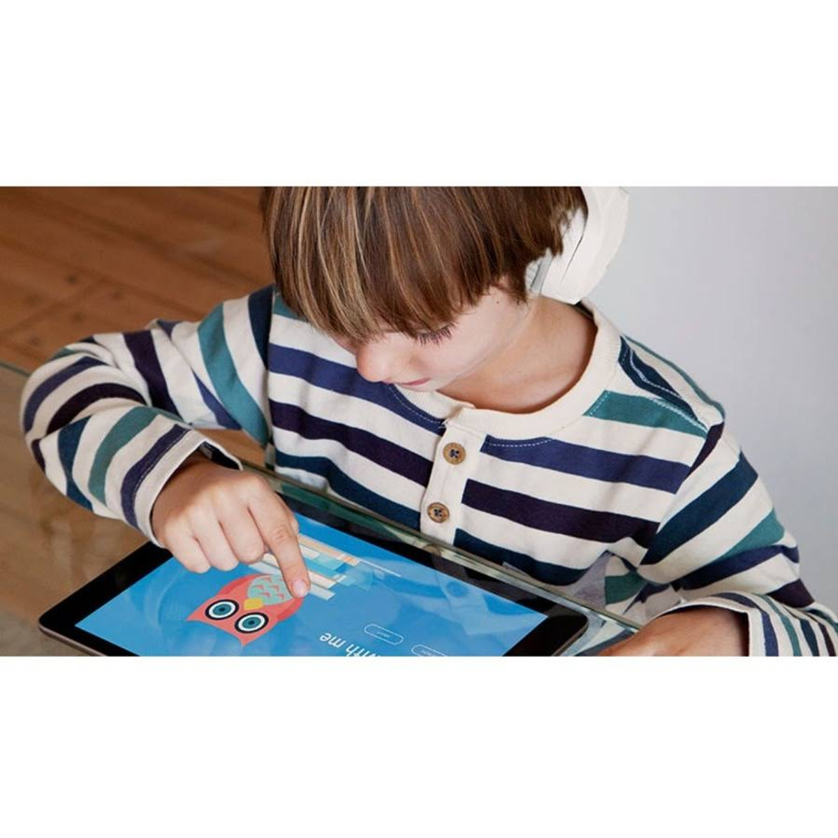 Dziecko używa tabletu, nosząc słuchawki. Tablet wyświetla aplikację.