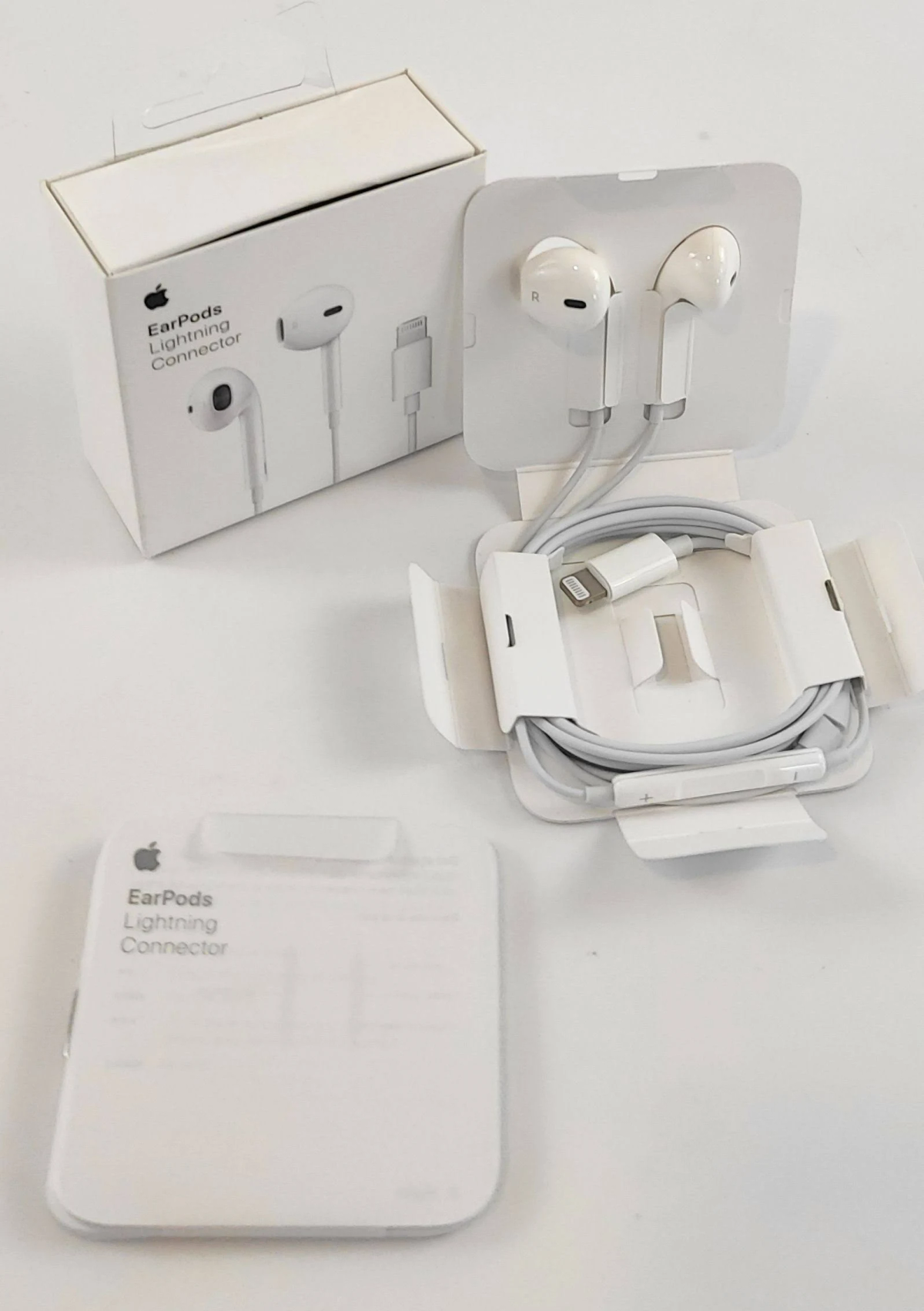 Białe słuchawki Apple EarPods w opakowaniu, w tym pudełko i otwarte etui ze słuchawkami.