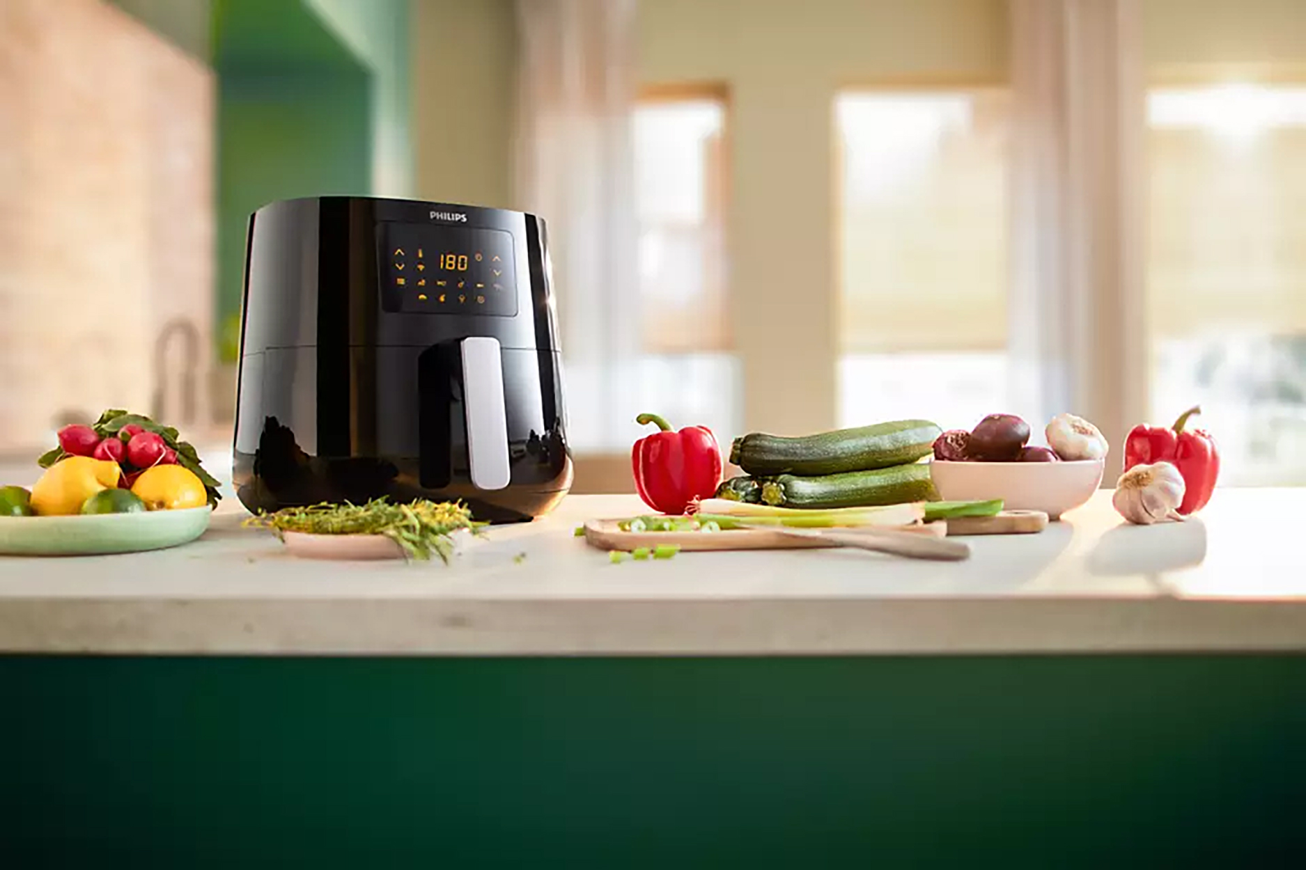 Zwarte airfryer met groenten op het aanrecht. Rode paprika's, courgette, uien en kruiden.