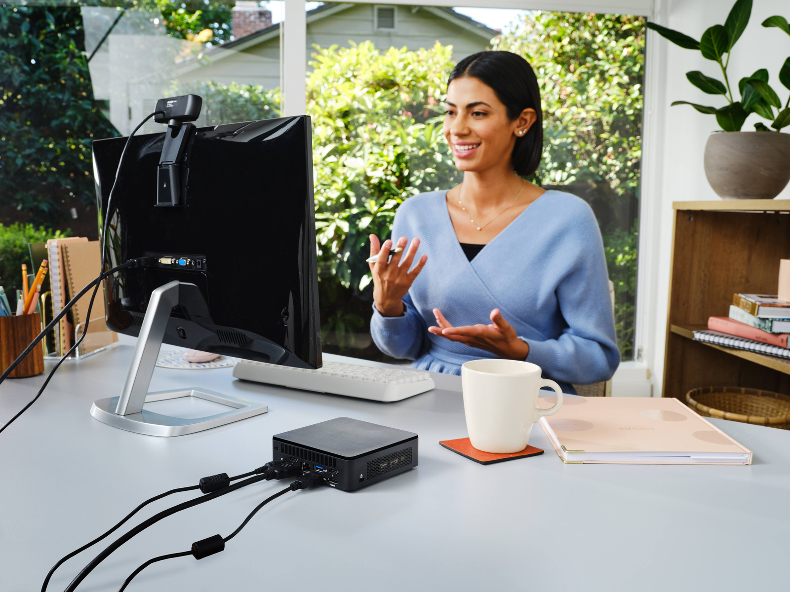 Donna alla scrivania con computer, webcam, monitor e accessori, che presenta una videochiamata.