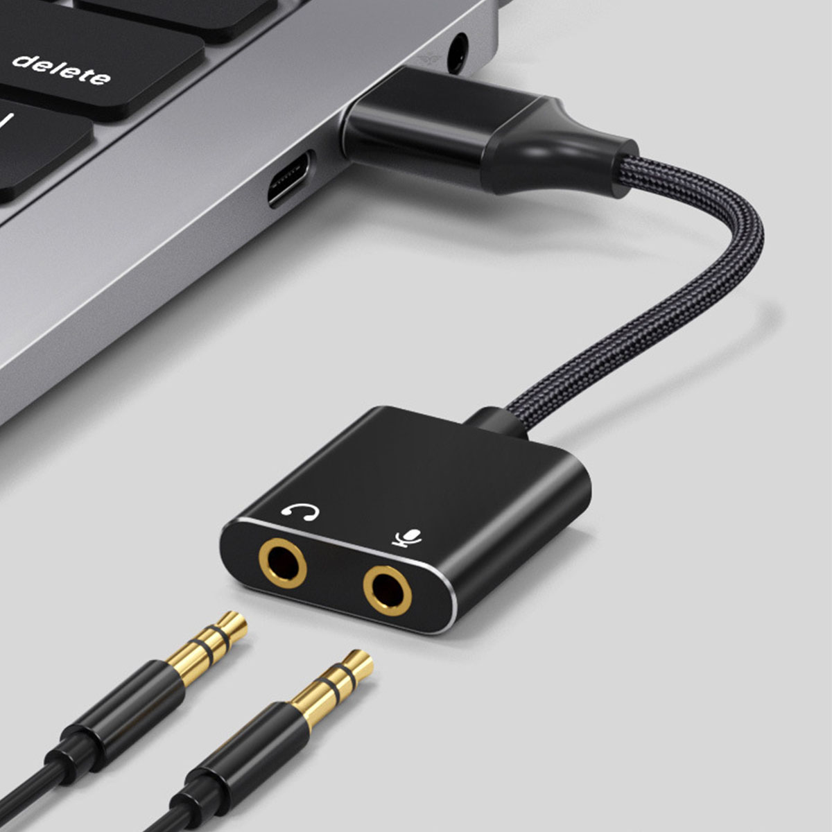 Ein schwarzer Audioadapter mit zwei goldfarbenen Audioanschlüssen und einem Mikrofonanschluss, eingesteckt in Laptop.