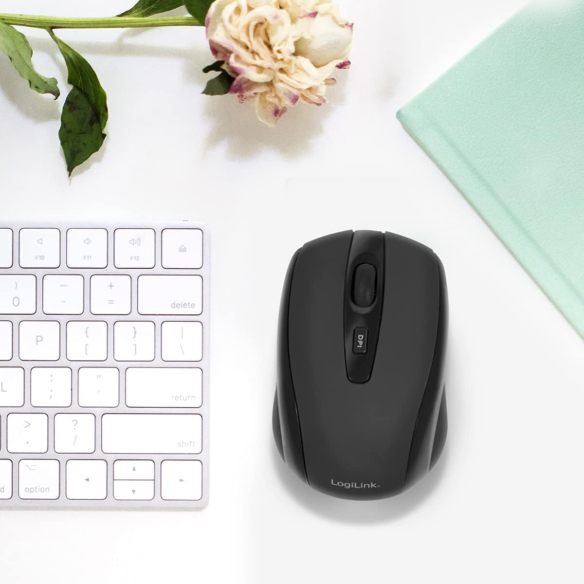 Schwarze drahtlose Maus mit weißer Tastatur und grünem Notizbuch. Weißer Hintergrund.
