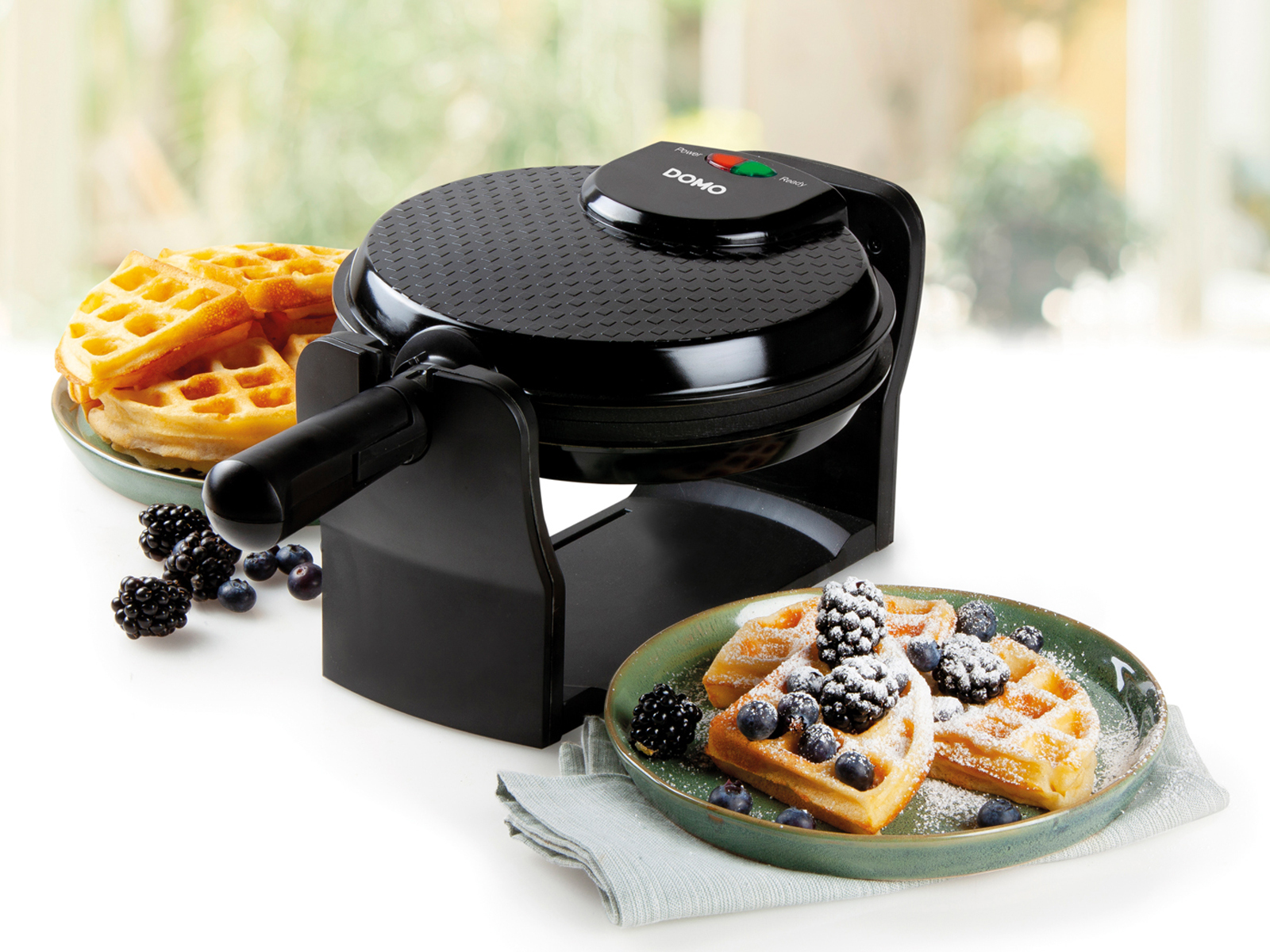 Schwarzer Waffeleisen mit Waffeln, Brombeeren und Blaubeeren auf dem Tisch.