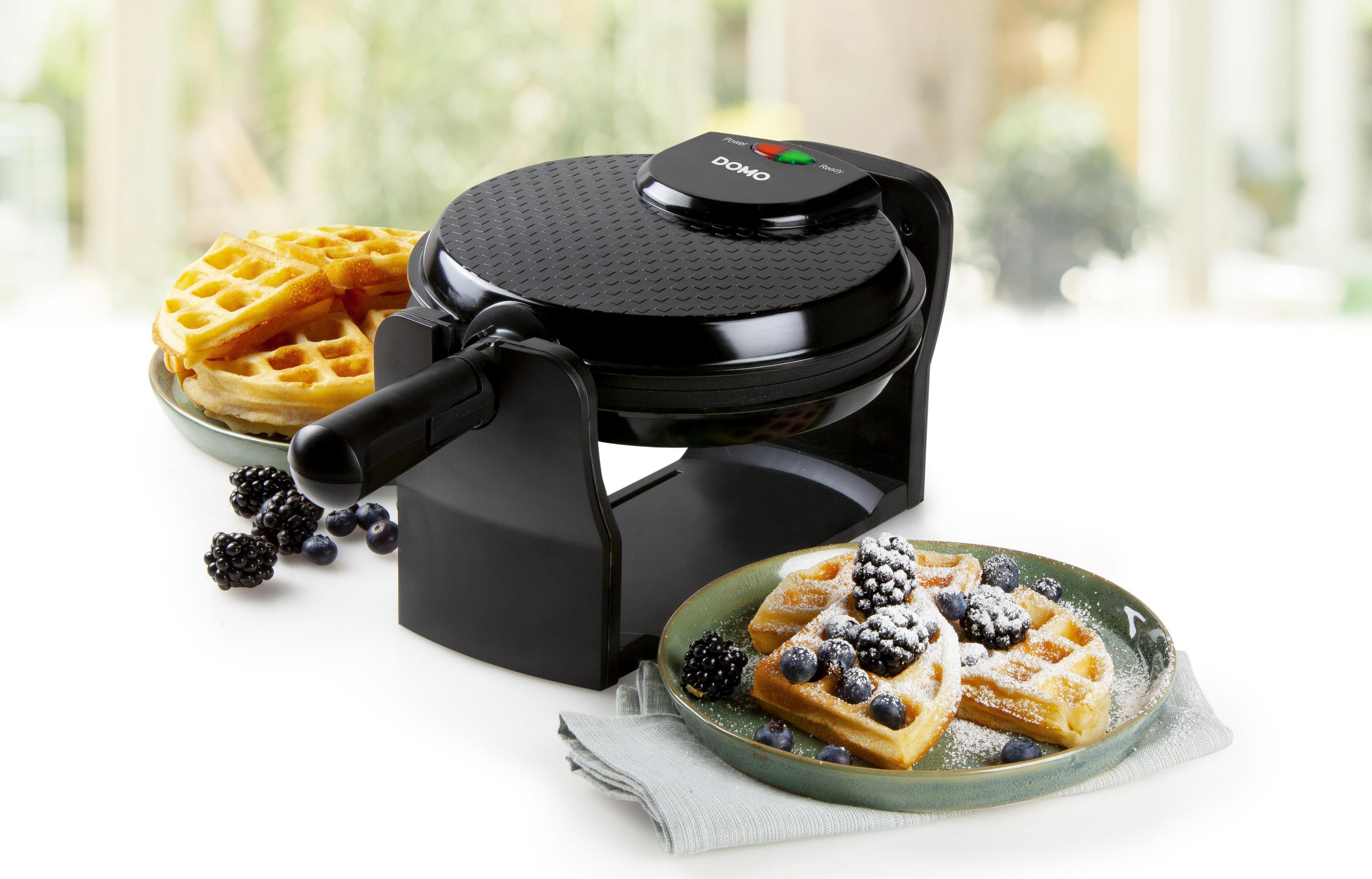 Schwarzer Waffeleisen mit Waffeln und Beeren auf einem Teller, in der Nähe eines Tellers mit Waffeln.