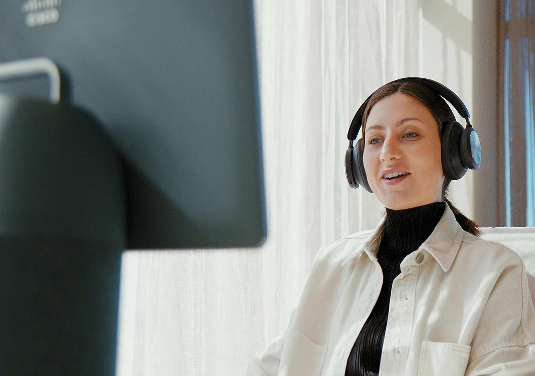 Eine Frau mit Kopfhörern in einem Videoanruf. Ein Computerbildschirm im Hintergrund.