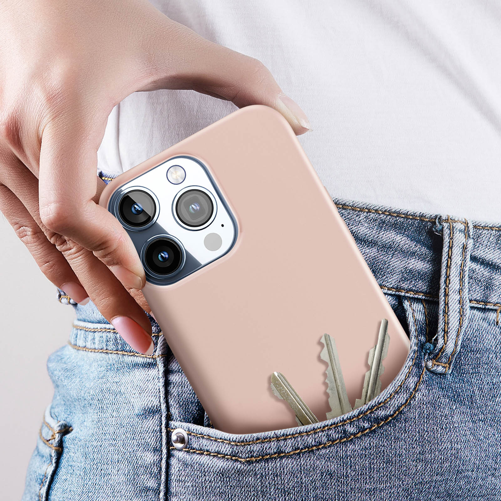 Una mano tiene una custodia per telefono color pesca in una tasca di jeans con chiavi all'interno.