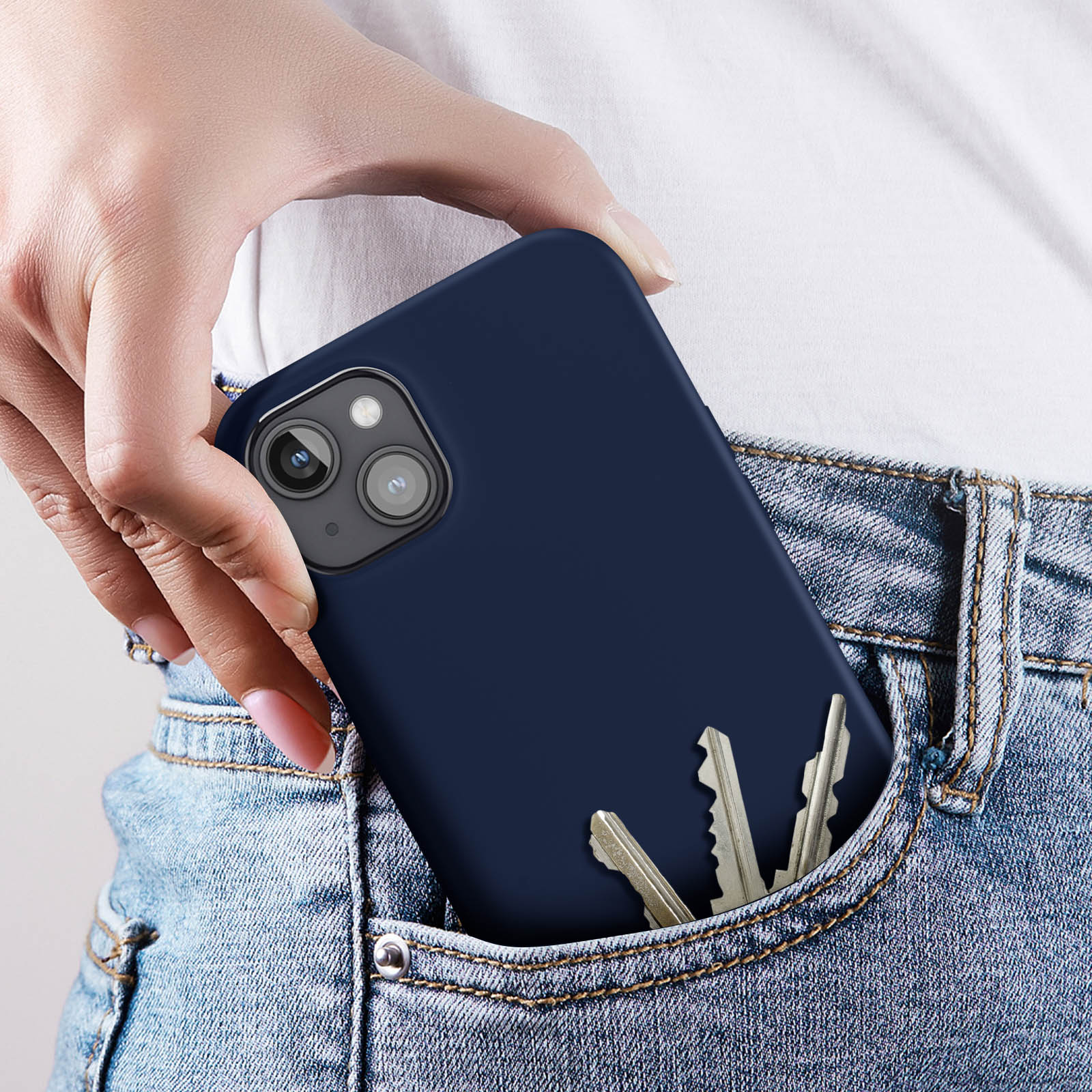 Una mano che tiene una custodia per telefono blu scuro. La custodia è nella tasca di un paio di jeans blu.