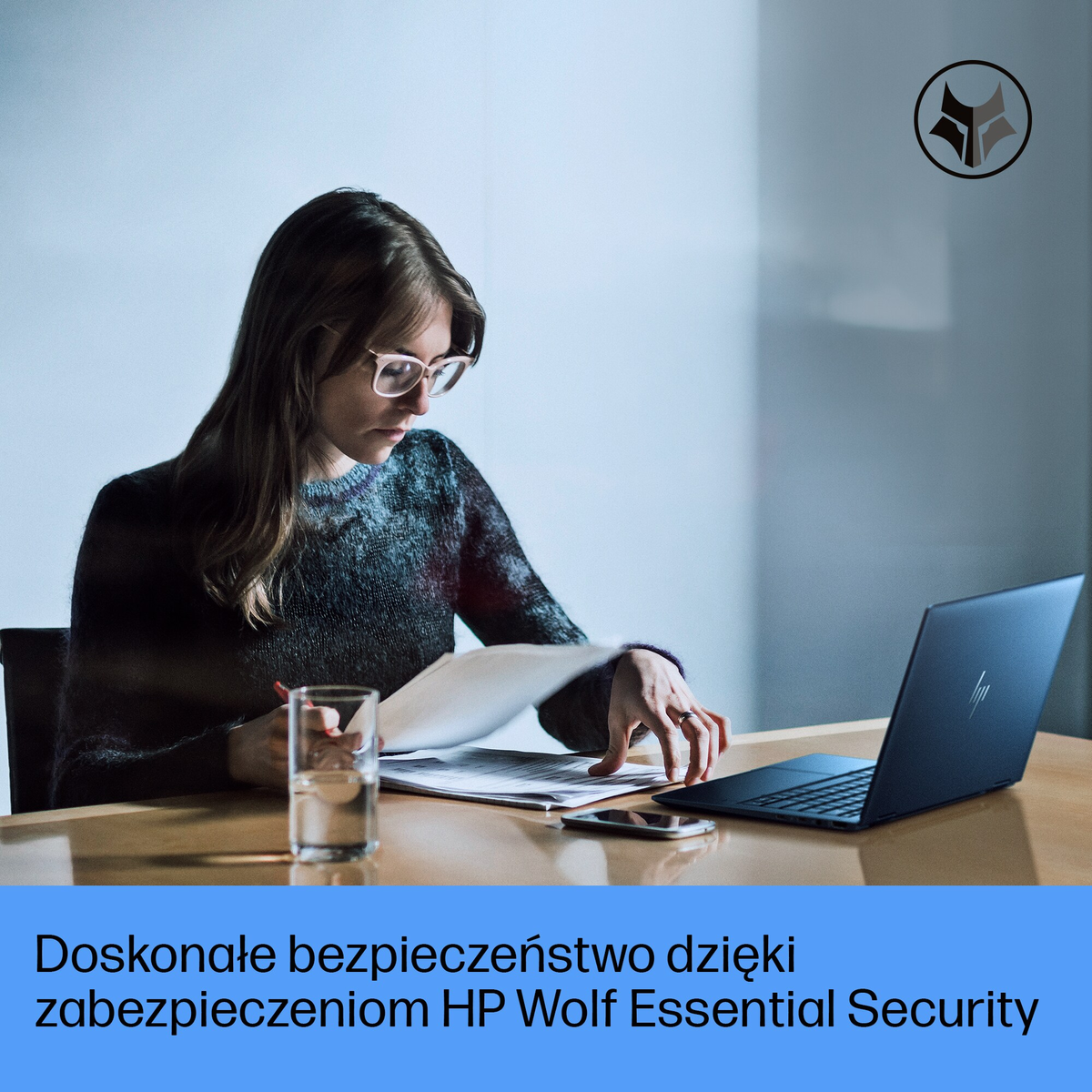 Kobieta w okularach przegląda papiery przy biurku z laptopem i szklanką wody.