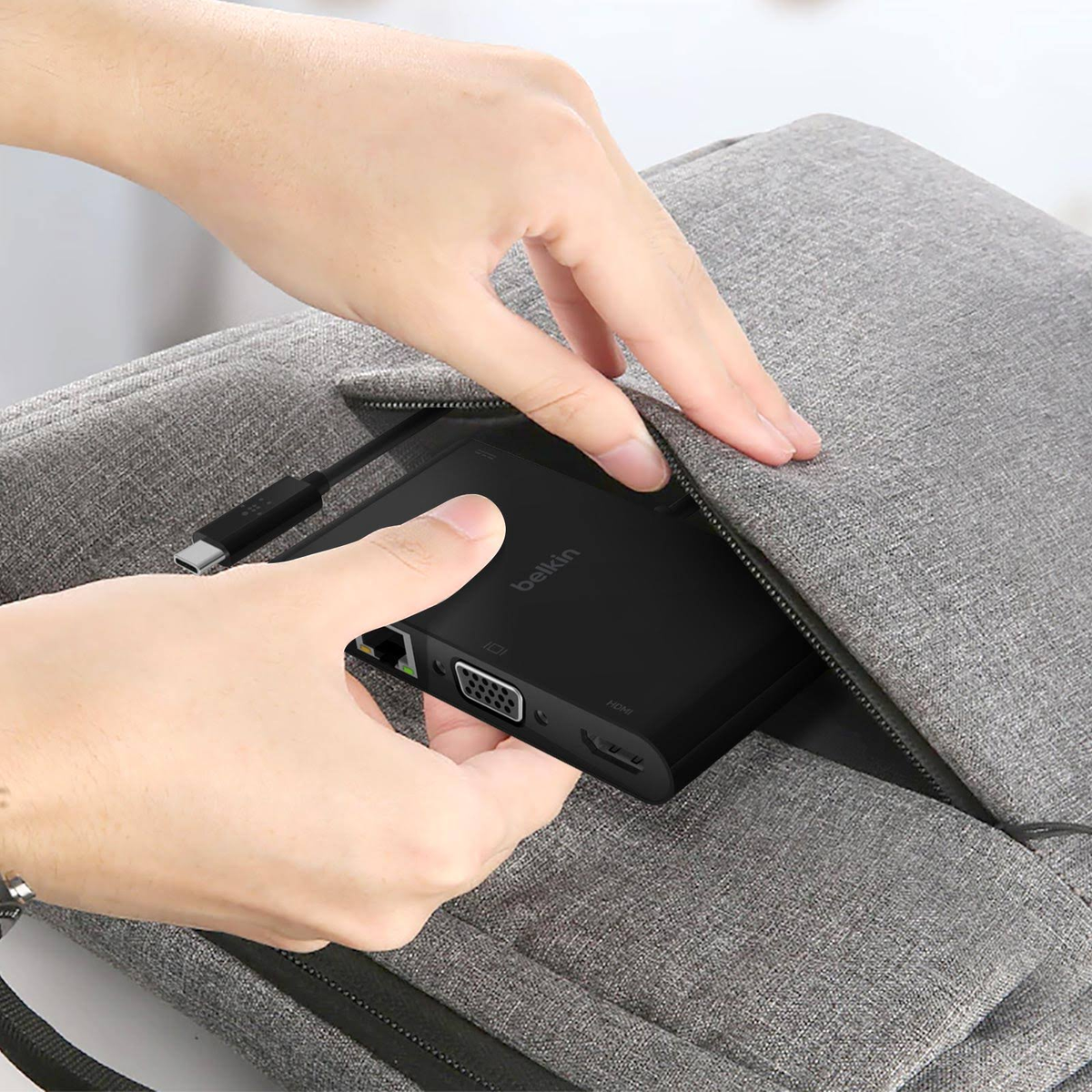 La mano di una persona estrae un hub Belkin da una borsa grigia. L'hub è nero con più porte.