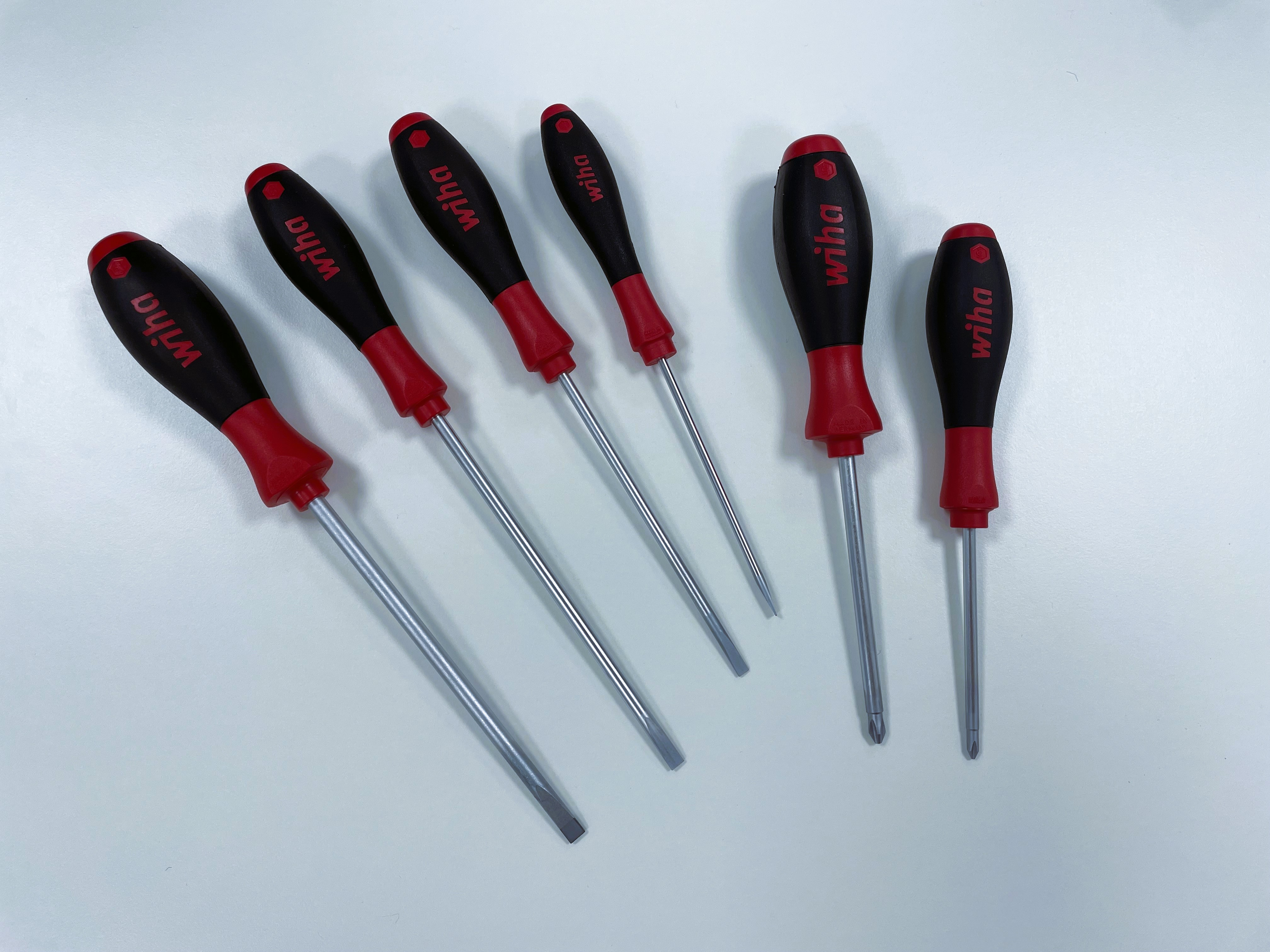 Sechs Schraubendreher mit rot-schwarzen Griffen, angeordnet auf weißer Oberfläche.