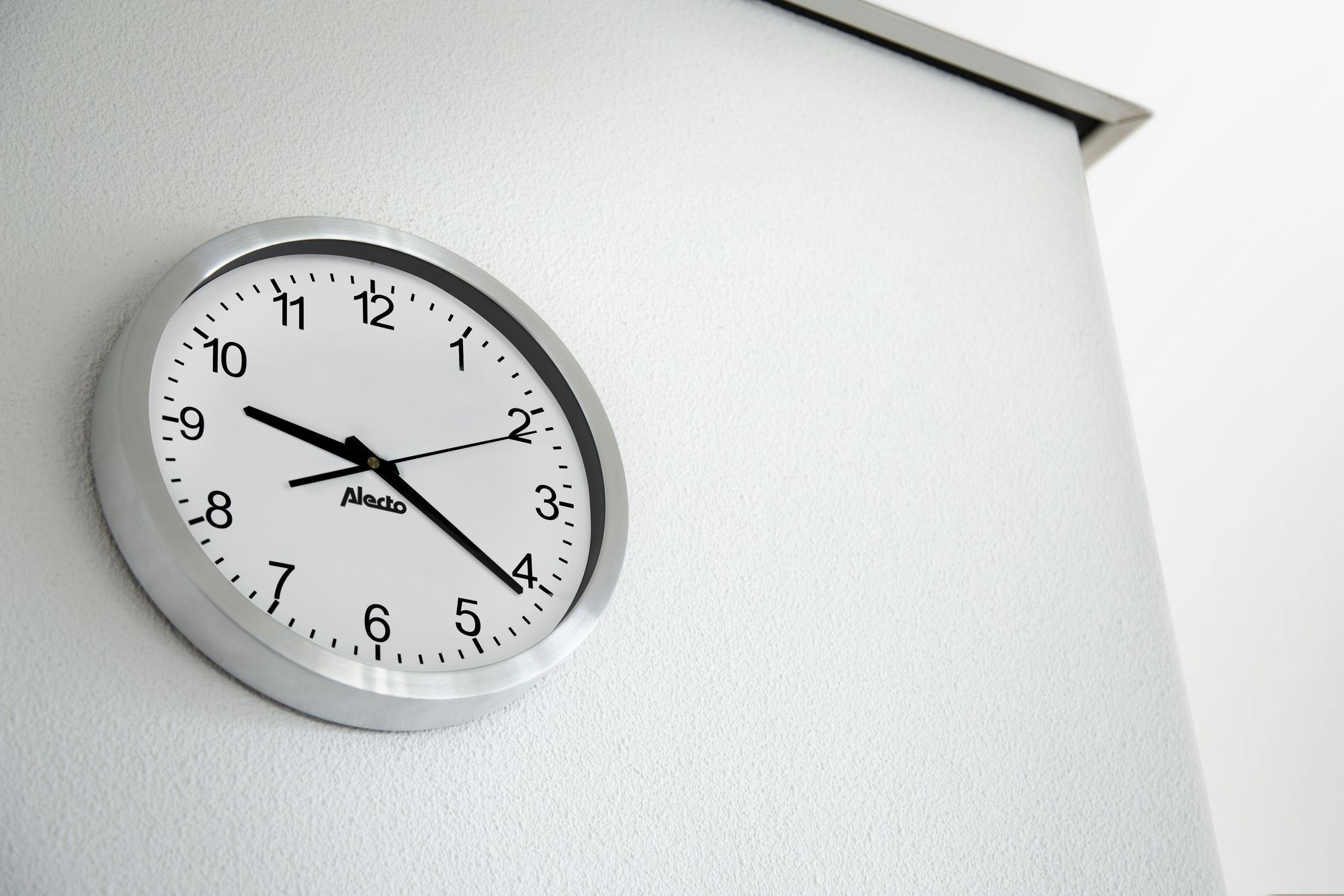 Eine runde Uhr an einer weißen Wand, mit silbernem Rahmen, die die Zeit anzeigt.