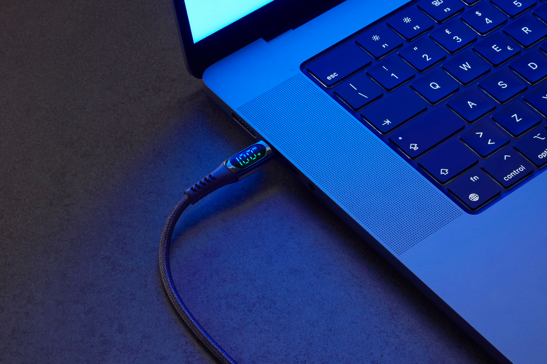 Laptop collegato con un cavo che mostra il 100%. Luce blu sulla tastiera e sul cavo.