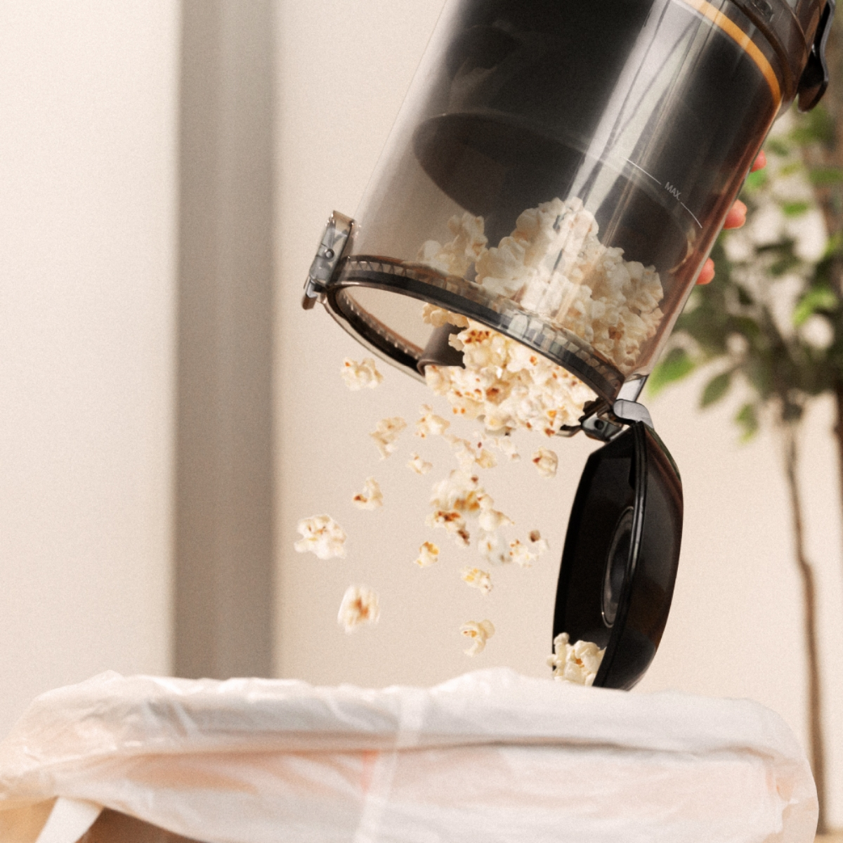 Palomitas de maíz vertiéndose de un recipiente negro a una bolsa de basura blanca. Fondo beige.