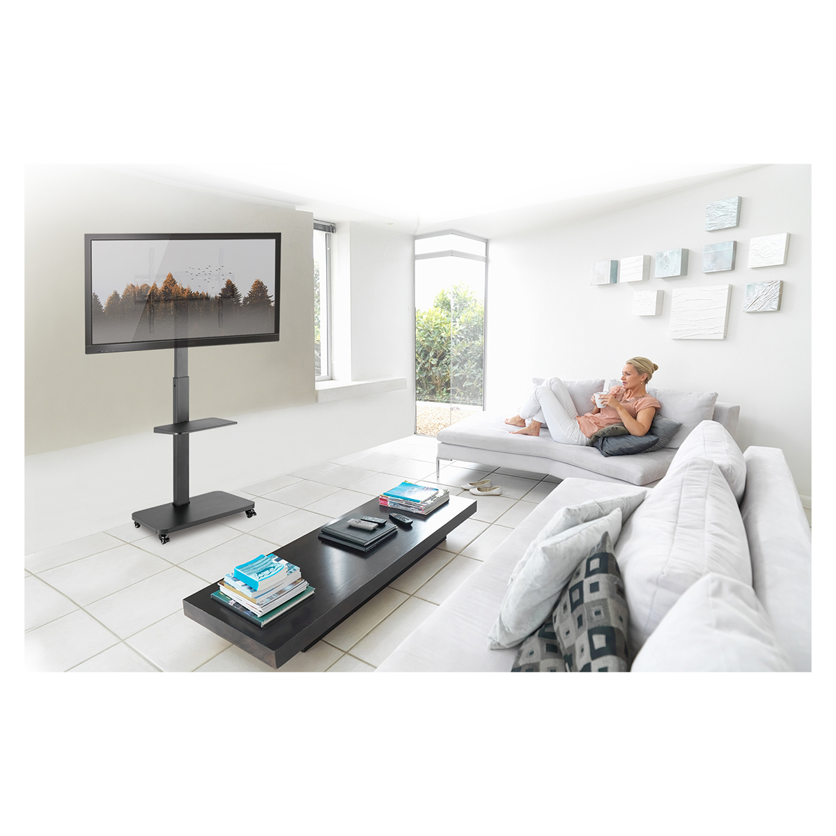 Wohnzimmer mit Fernseher auf einem Ständer, einer Frau auf einem Sofa und einem Couchtisch mit Büchern.