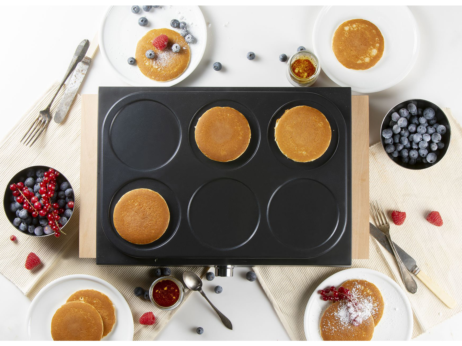 Pfannkuchen auf einer schwarzen Grillplatte, serviert mit Beeren und Gewürzen.
