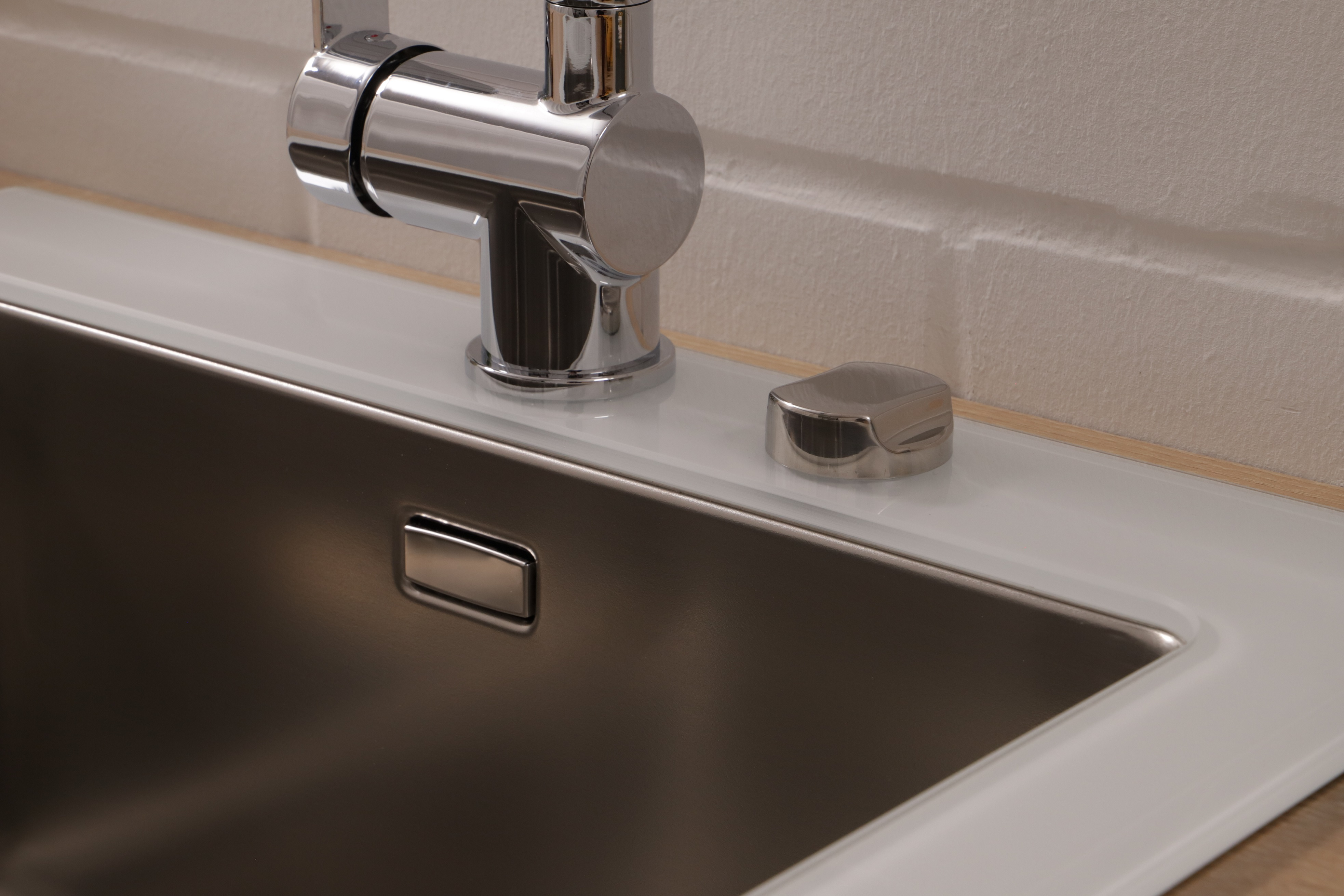 Chrom-Wasserhahn und ein Edelstahlbecken. Rechts neben dem Wasserhahn befindet sich ein kleiner Chromknopf.