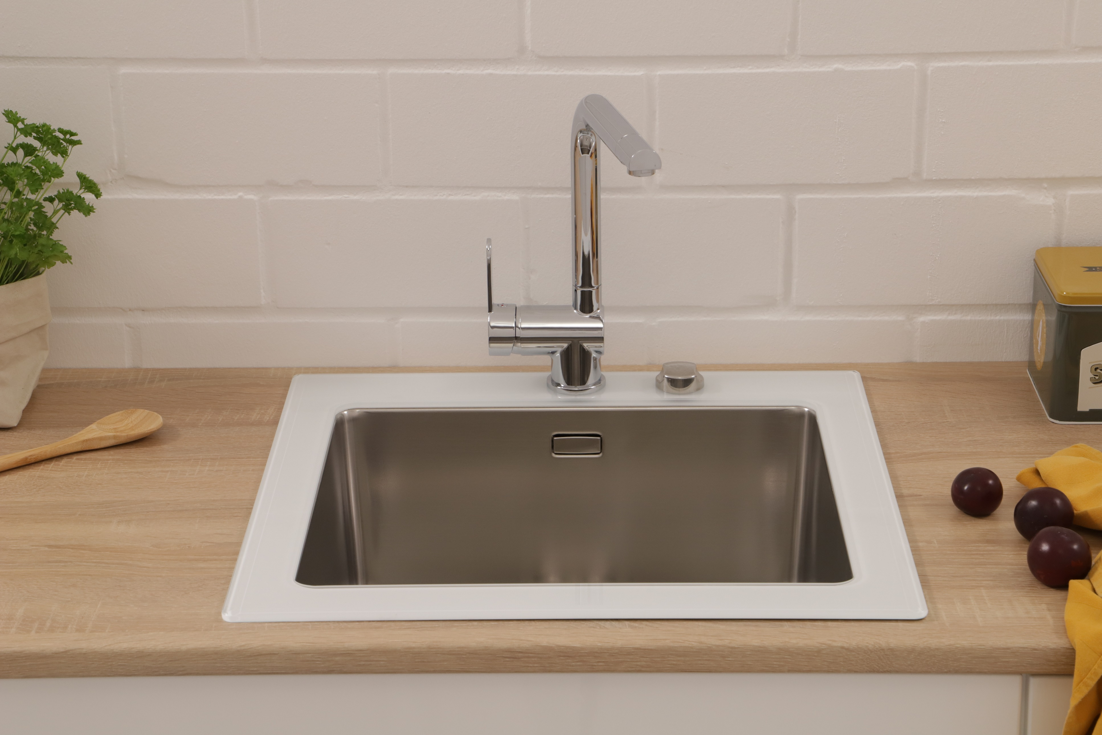 Ein Edelstahlwaschbecken mit Chromarmatur, eingebaut in eine Holz-Arbeitsplatte, mit Pflaumen und Kräutern im Hintergrund.