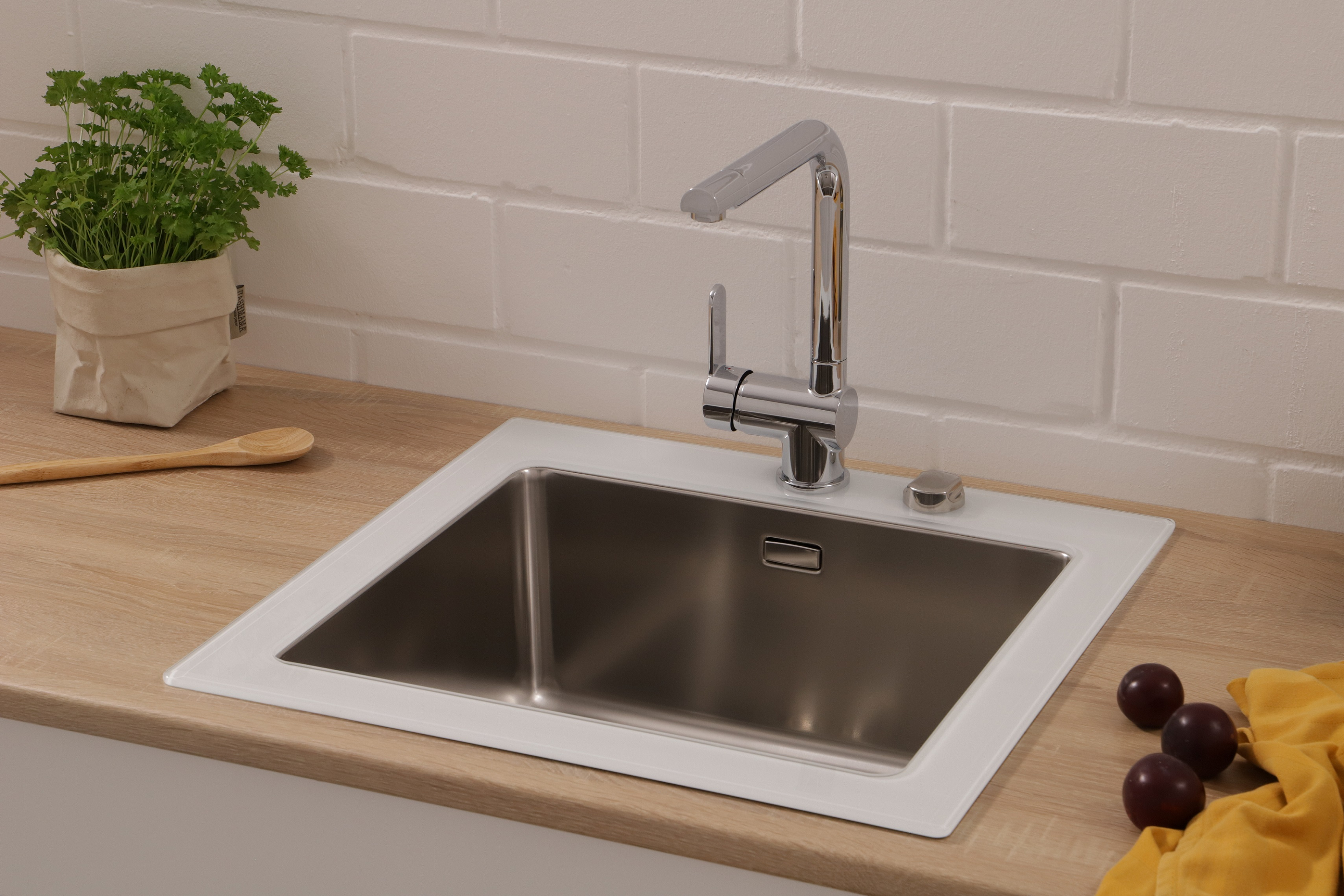 Ein Edelstahl-Küchenbecken mit Chromarmatur. Eine Holztheke und Pflaumen sind zu sehen.