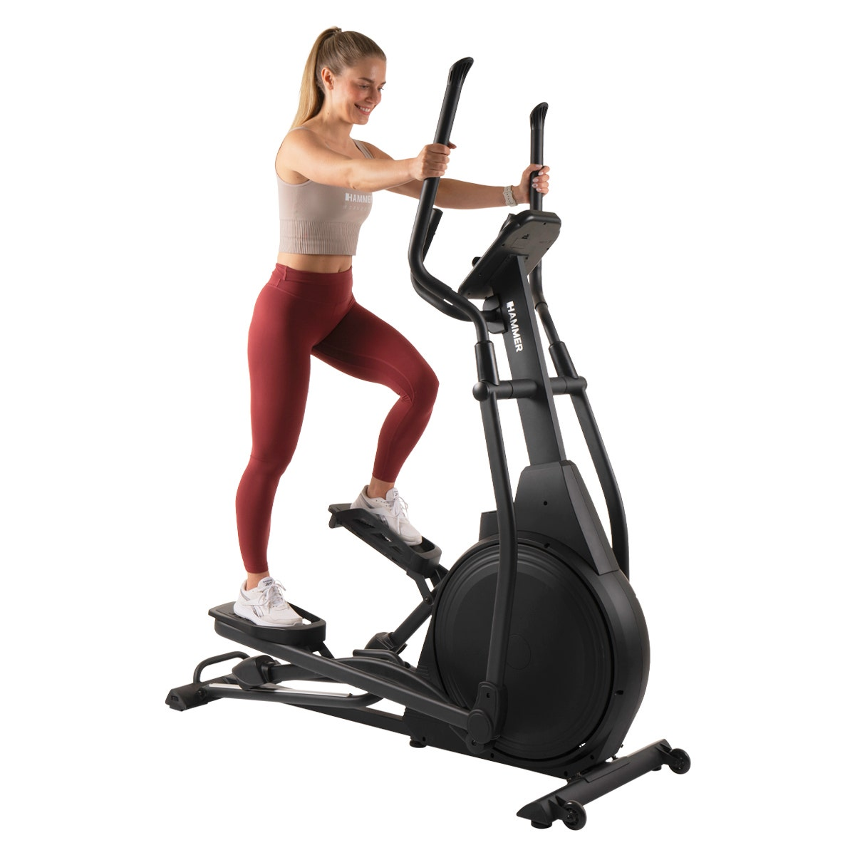 Frau auf einem Crosstrainer, trägt rote Leggings. Schwarze Maschine, weißer Hintergrund.