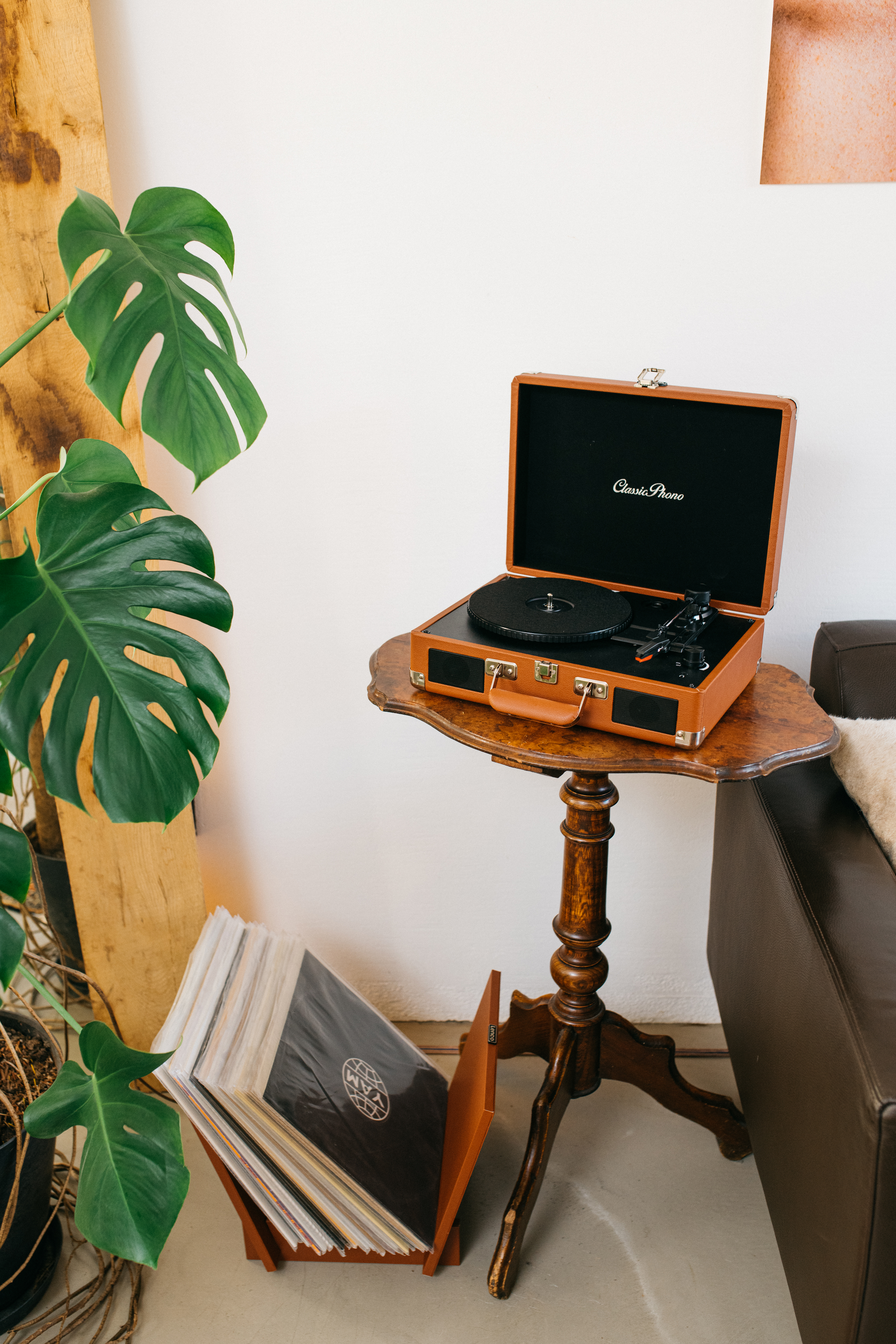 Brązowy gramofon w stylu walizki stoi na drewnianym stole. Płyty są wystawione na podłodze.