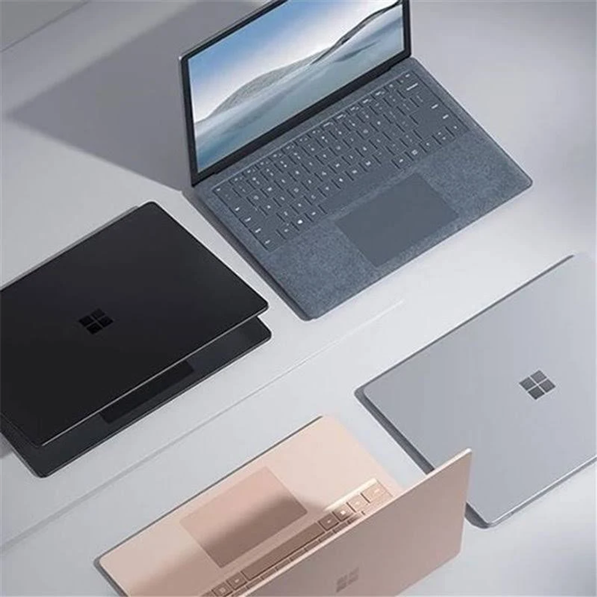 Vier Laptops in verschiedenen Farben auf einer Oberfläche angeordnet. Einer ist geöffnet, die Tastatur sichtbar.