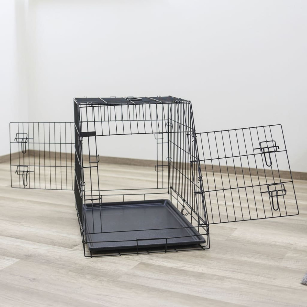 Schwarze Metall-Hundebox mit offenen Türen auf hellem Holzboden.