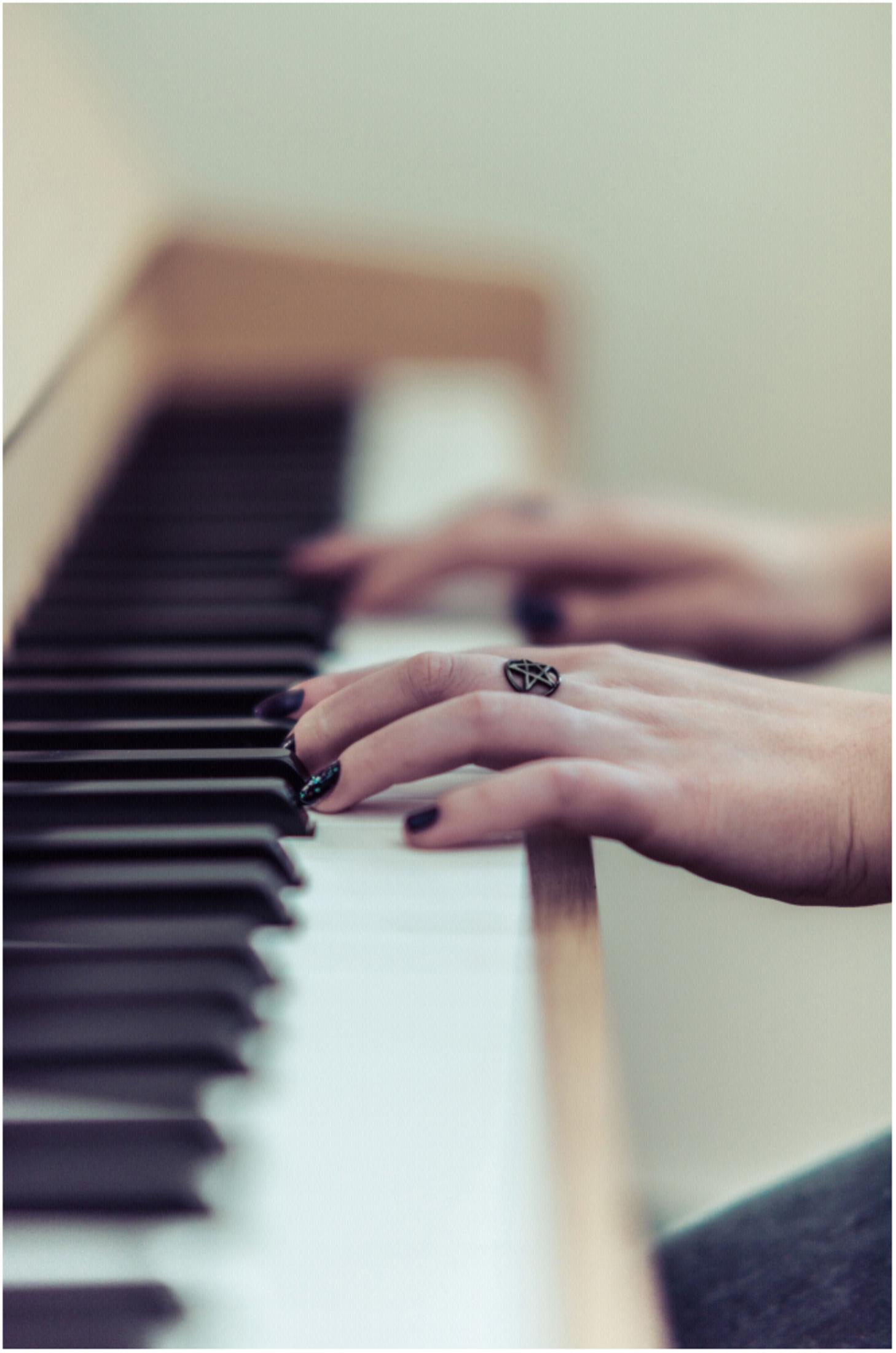 Dłonie grające na pianinie, czarne paznokcie i pierścionek z gwiazdą na palcu.