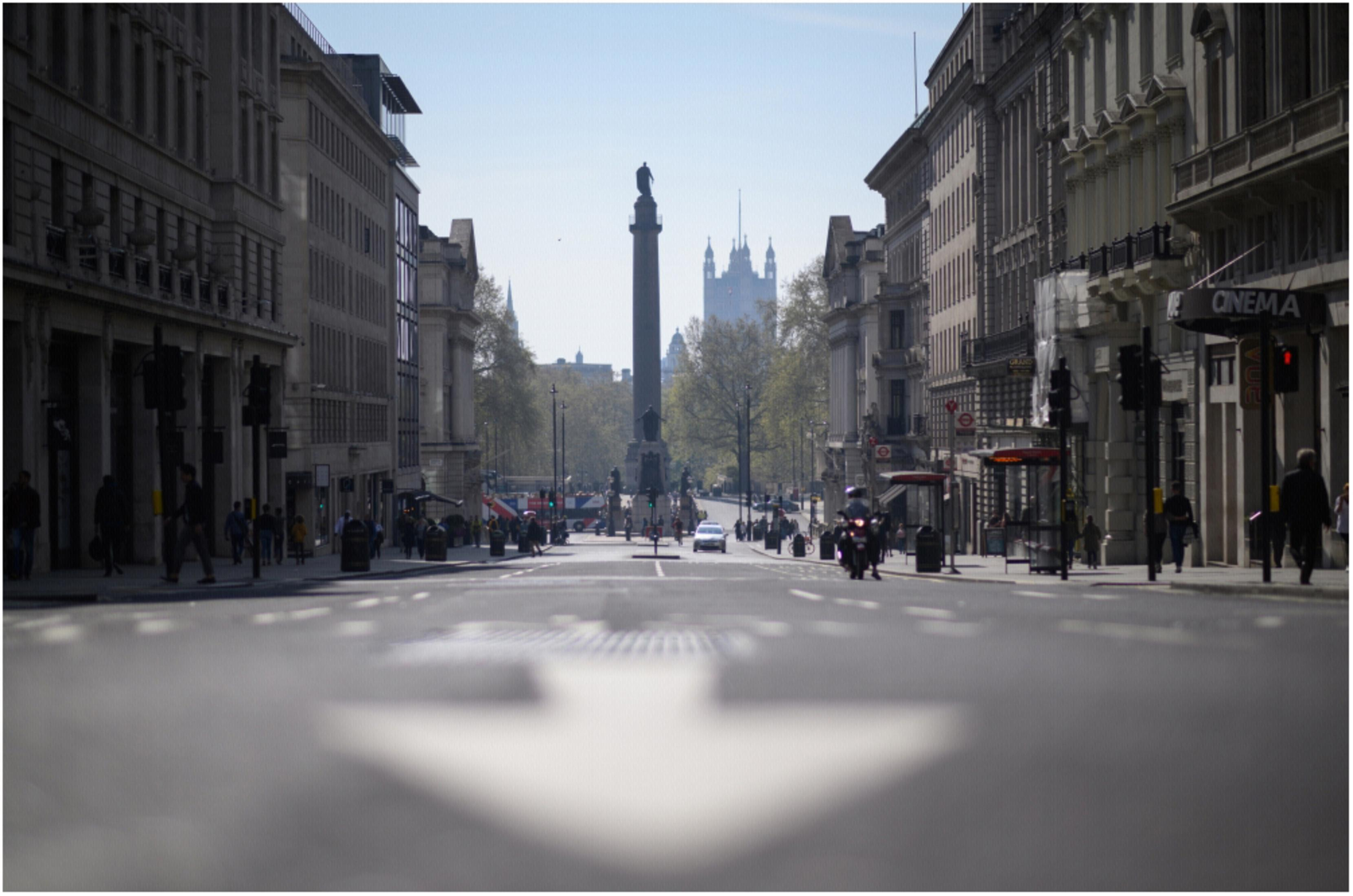 Straßenszene mit Gebäuden auf beiden Seiten und einem Denkmal in der Ferne.