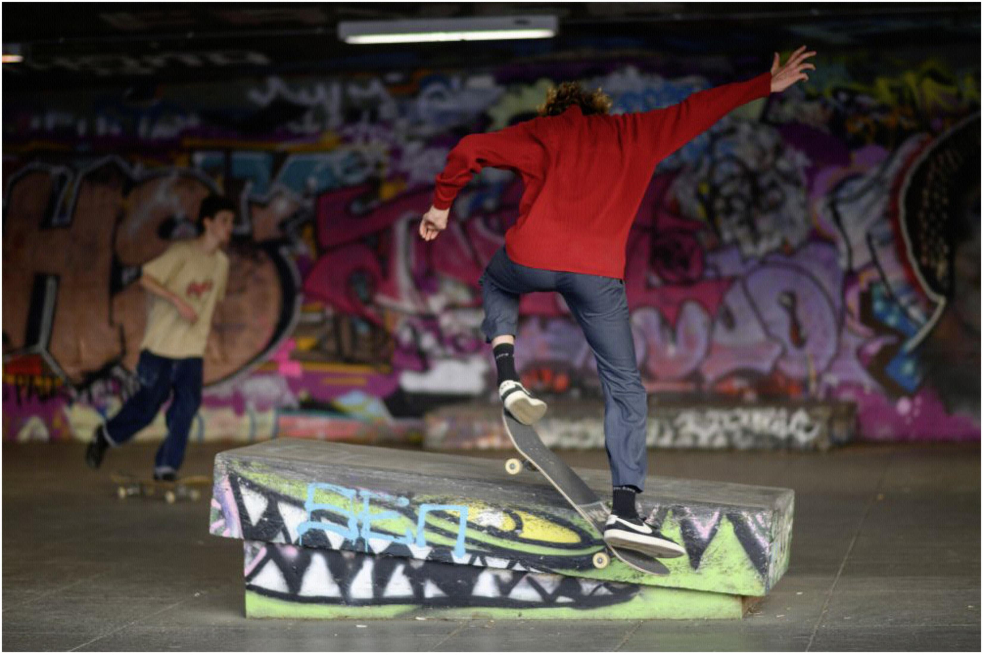 Ein Skateboarder springt über einen Betonblock mit Graffiti in einem Skatepark.