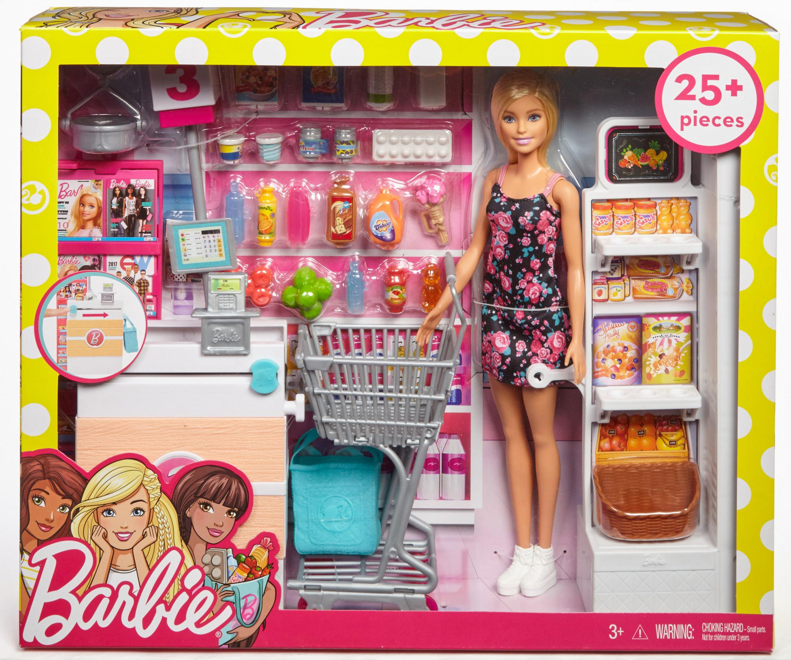 Lalka Barbie w kwiecistej sukience stoi w ekspozycji sklepu spożywczego z zabawkami. Wózek i półki z produktami spożywczymi.