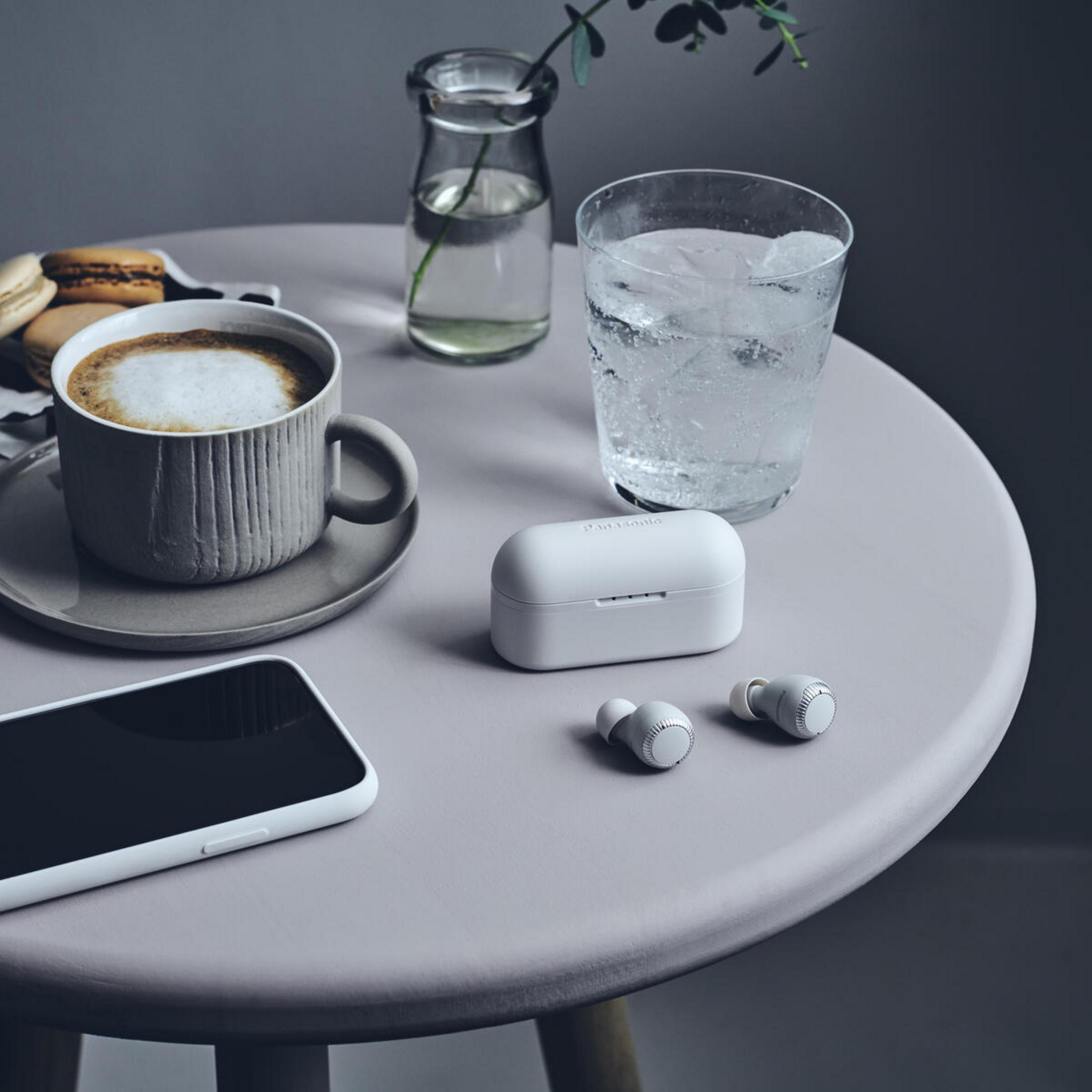 Mesa con café, auriculares, agua y un teléfono. Macarons a un lado.