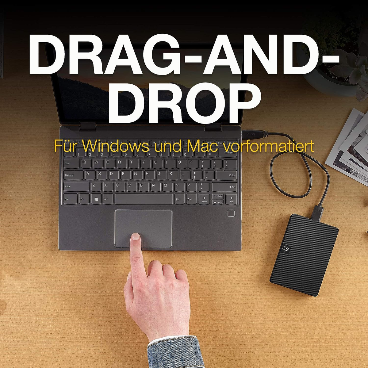 Laptop podłączony do czarnego dysku twardego. Dłoń dotykająca touchpada.