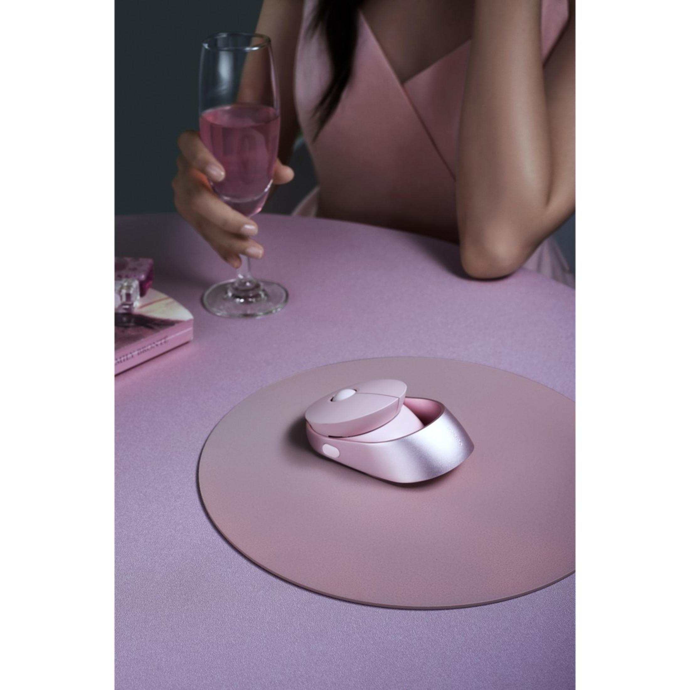 Różowa mysz i etui na różowej macie. Osoba trzyma szklankę z różowym płynem. Fioletowy stół.