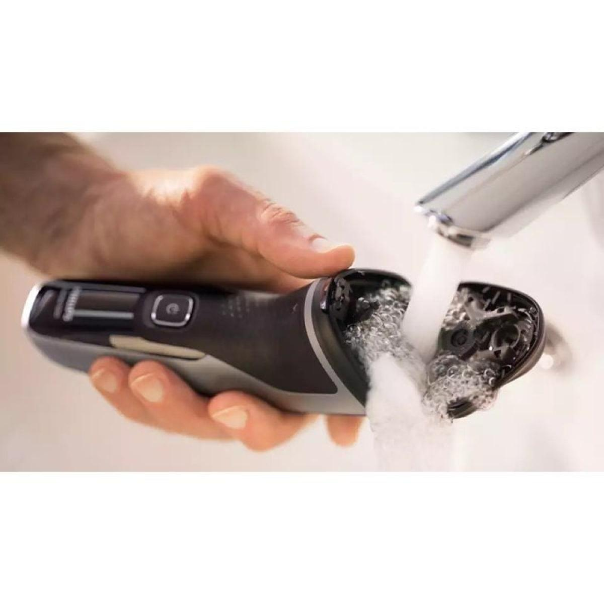 Mano di uomo che tiene un rasoio elettrico nero sotto l'acqua corrente. La testina è aperta.