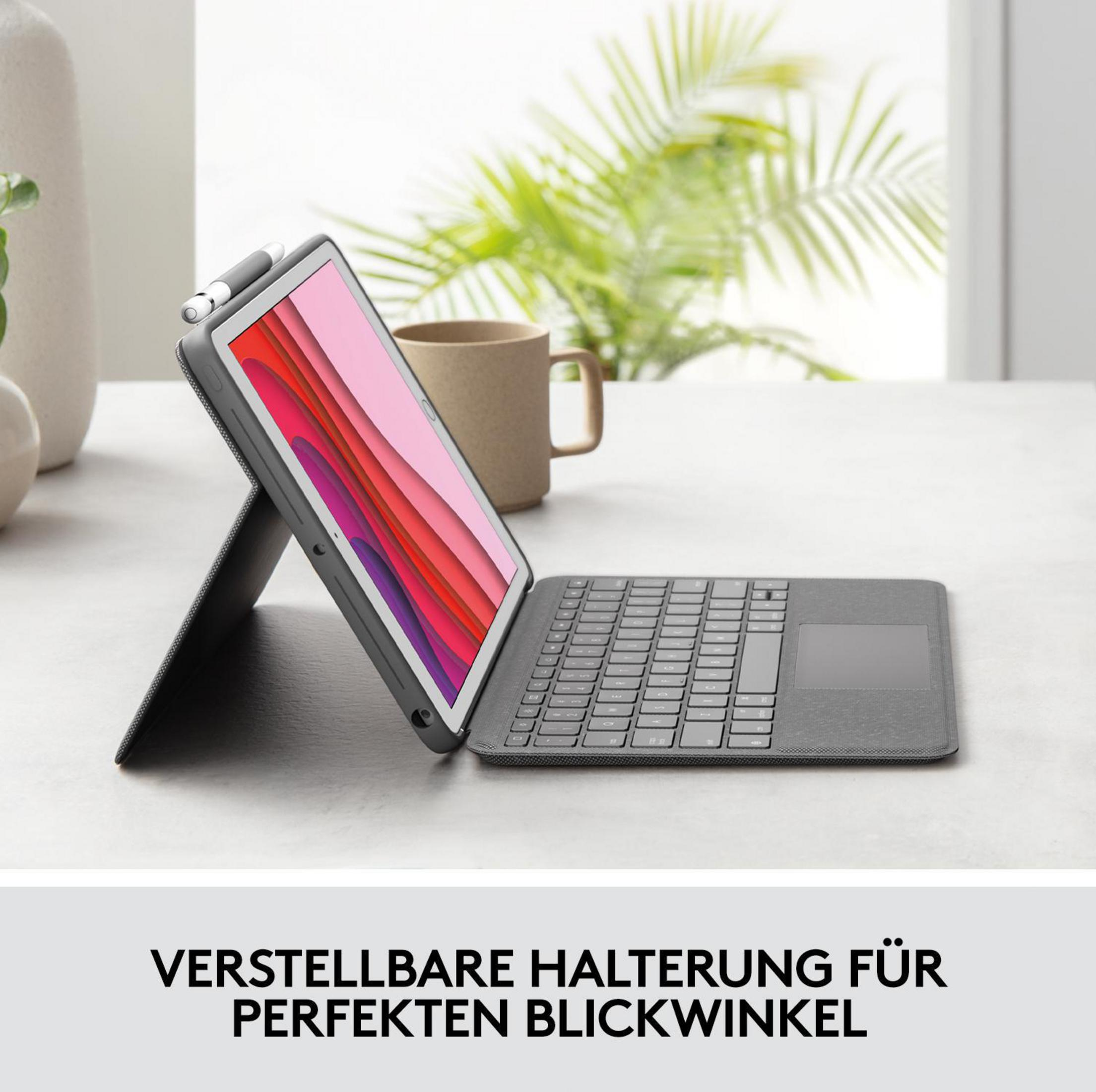 Tablet na szarej obudowie klawiatury, podparty piórem. Kubek w tle.