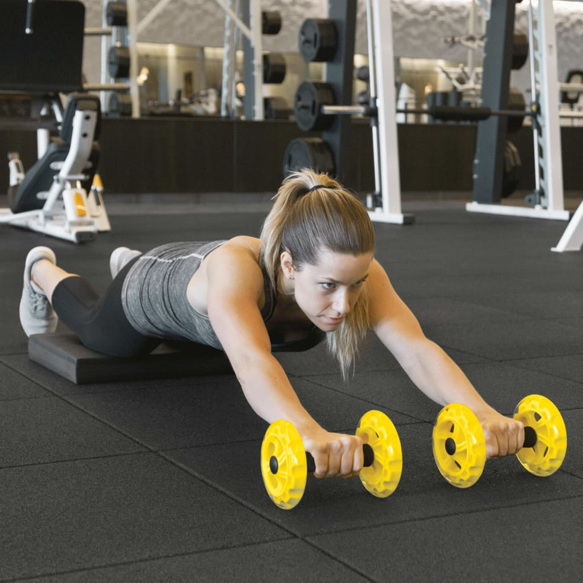 Una donna si allena in palestra, usando ruote ginniche gialle su un tappetino.