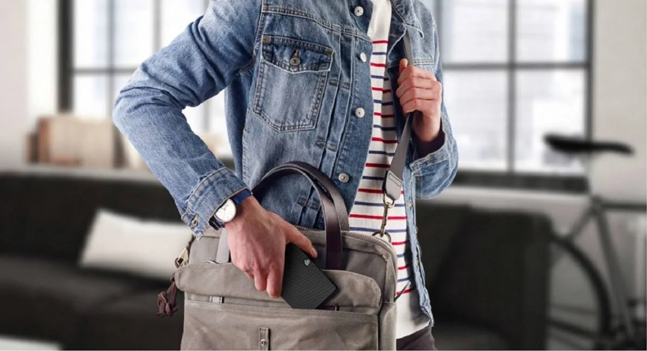 Mężczyzna w dżinsowej kurtce wkłada telefon do torby. Zegarek na jego nadgarstku.